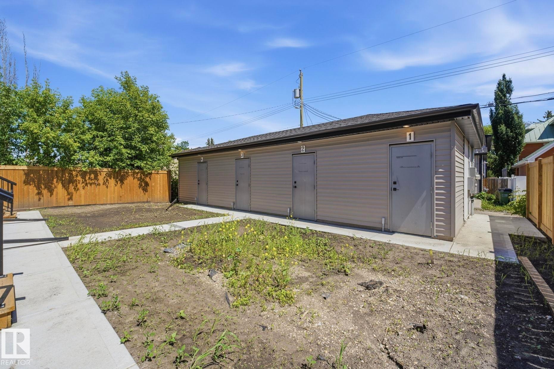 Building exterior featuring beige siding, multiple entry doors with overhead lighting, and a dark shingle roof - 11007 132 Street, Edmonton, AB