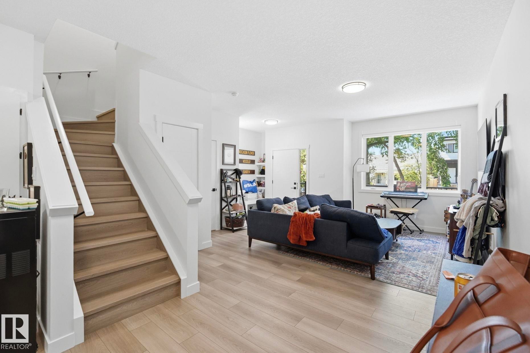 Open-concept living space featuring light wood-finish flooring, white walls, and a prominent staircase with white risers and wood treads - 11007 132 Street, Edmonton, AB