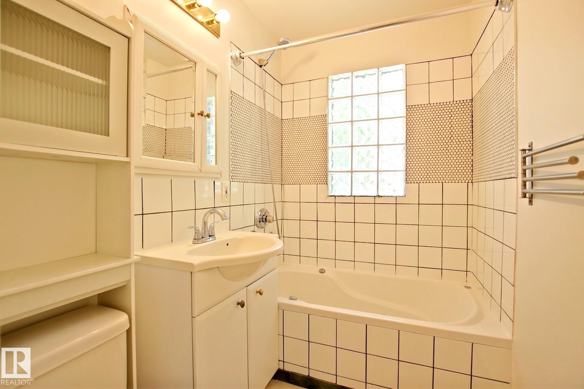 Bathroom featuring a white bathtub, ceramic tile walls, and a glass block window - 11242 56 Street, Edmonton, AB