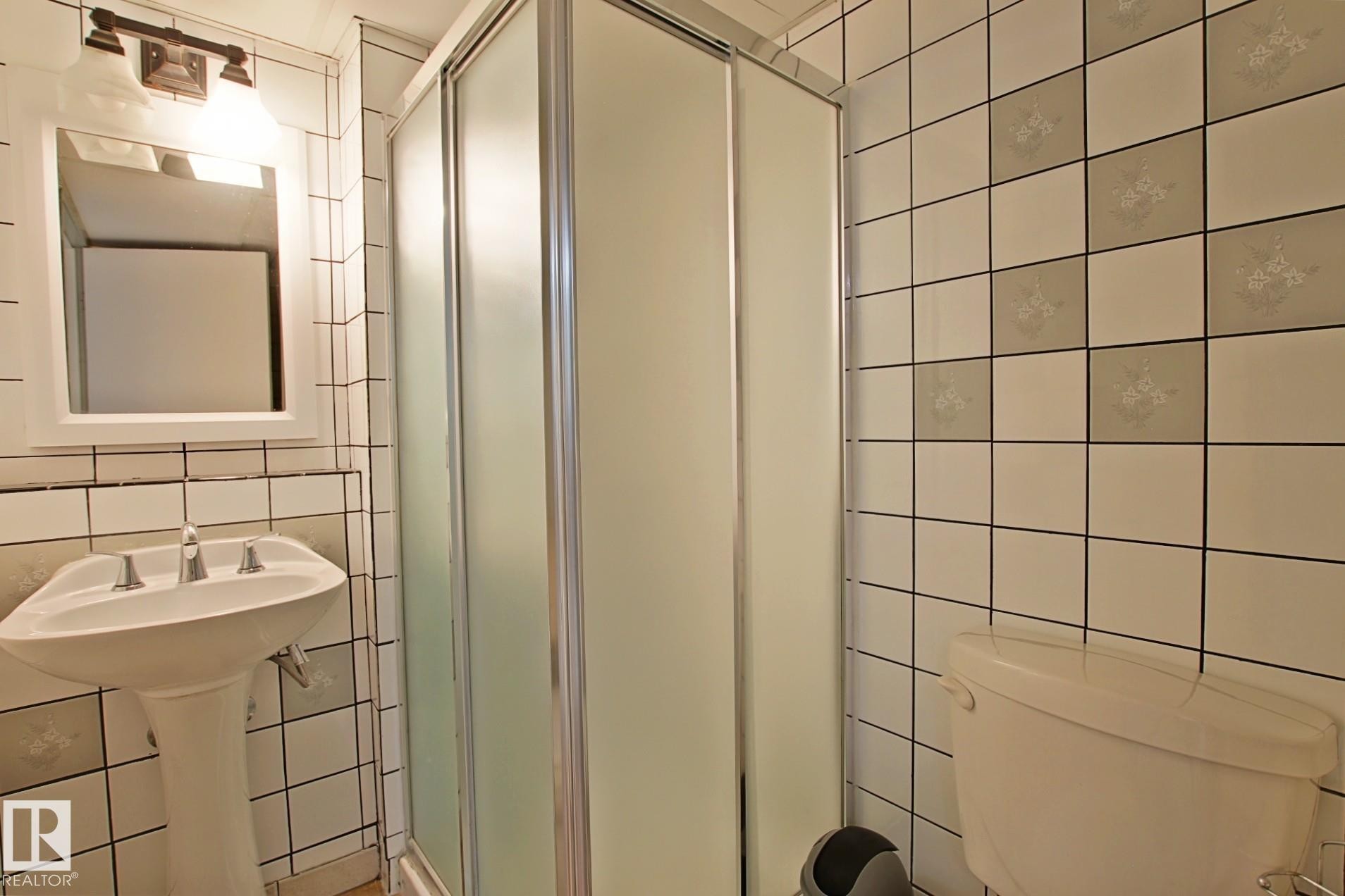 Bathroom with a pedestal sink, white subway tile, patterned accent tiles, a shower enclosure with frosted glass, and a toilet - 11242 56 Street, Edmonton, AB