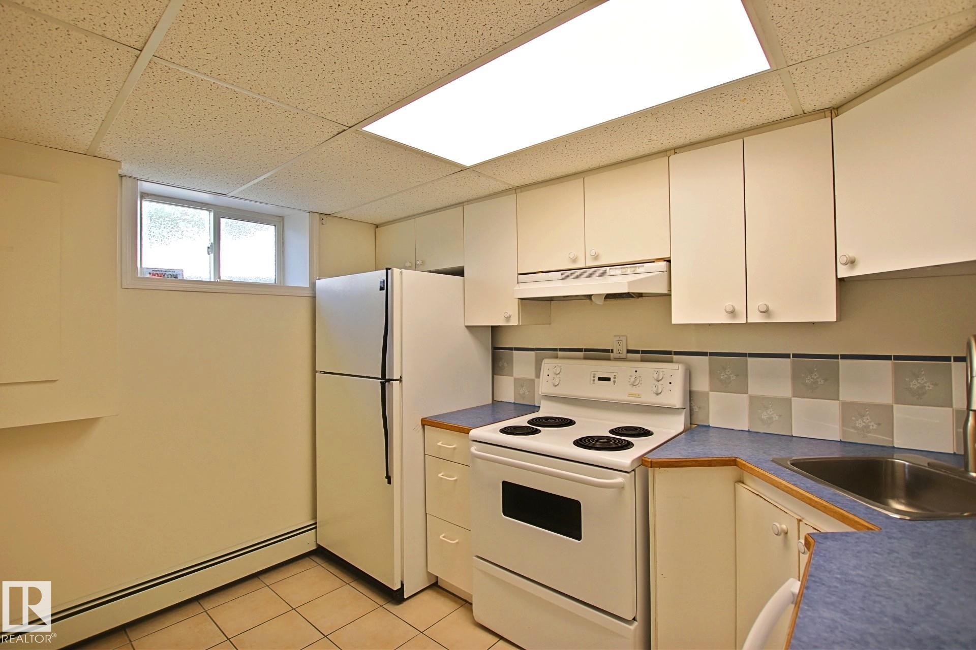 Kitchen featuring a white electric range, white upper and lower cabinetry, and a stainless steel sink - 11242 56 Street, Edmonton, AB