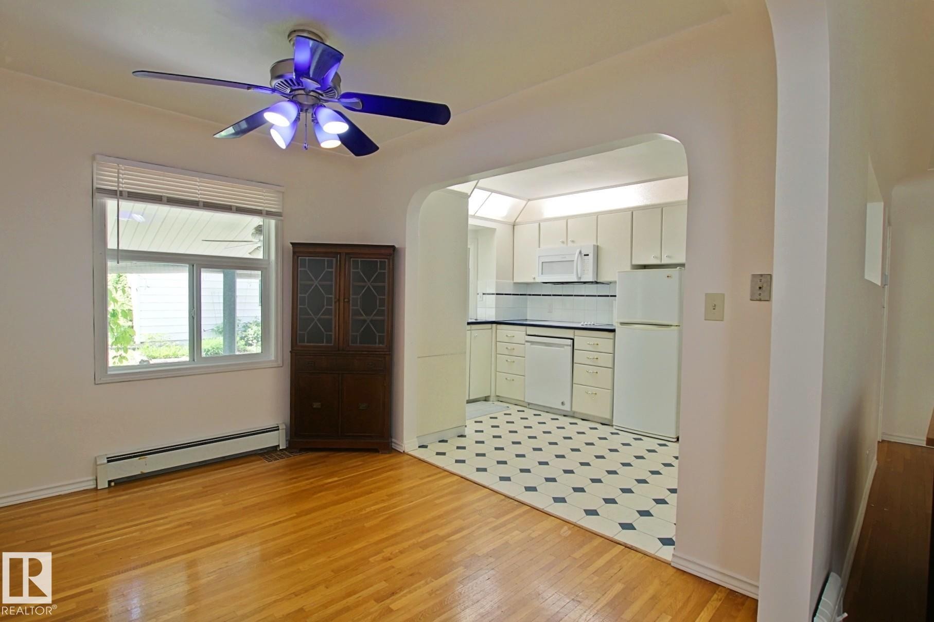 Bright kitchen with white cabinetry and appliances, black countertops, and a checkered tile floor - 11242 56 Street, Edmonton, AB