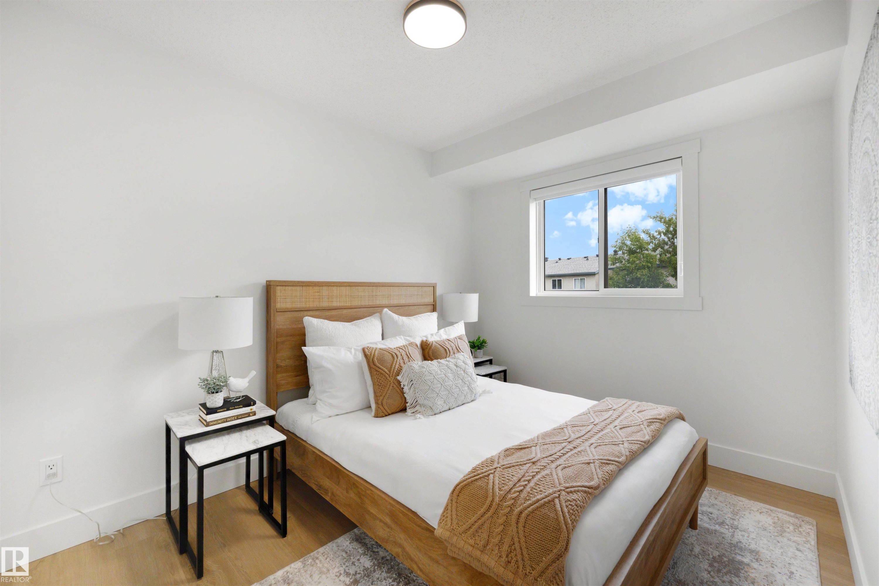 Light-filled bedroom featuring wood-finish flooring, a contemporary window, and crisp white walls - 12611 47 Street, Edmonton, AB