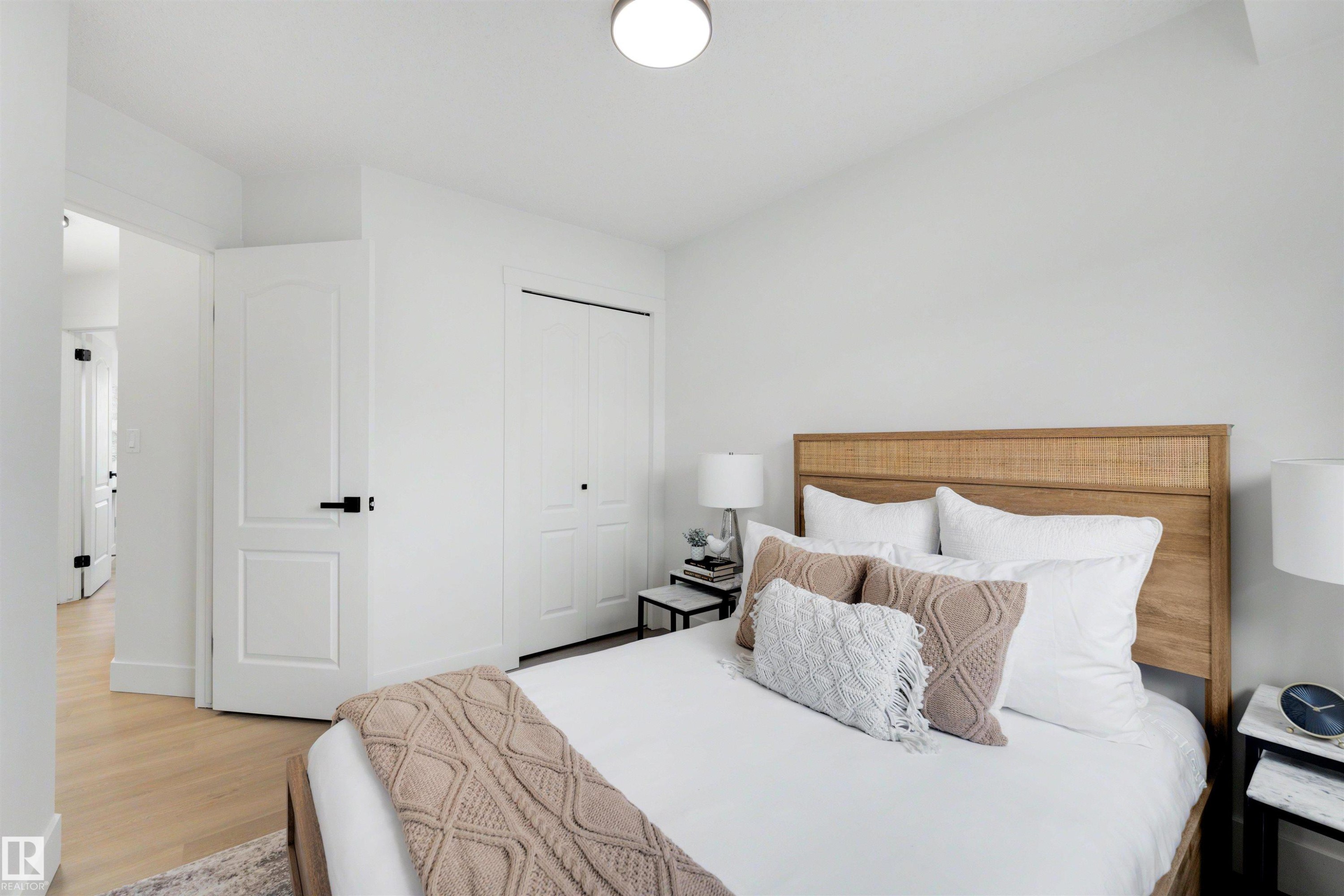 Bright interior space featuring light wood-finish flooring, a white paneled door with matte black hardware, and a closet with bi-fold doors - 12611 47 Street, Edmonton, AB