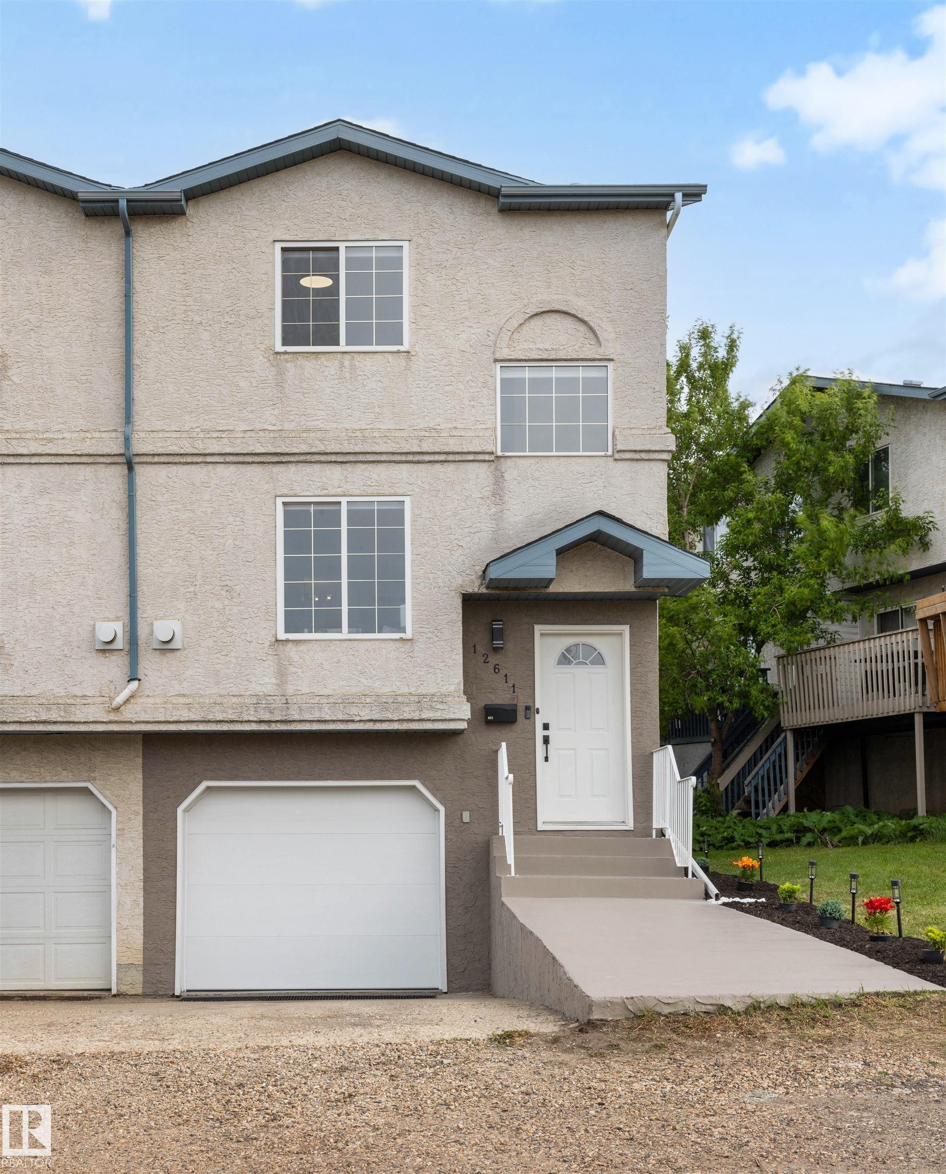 Three-story stucco exterior featuring a prominent arched window, white entry door with frosted glass, and an attached garage with a modern white door - 12611 47 Street, Edmonton, AB