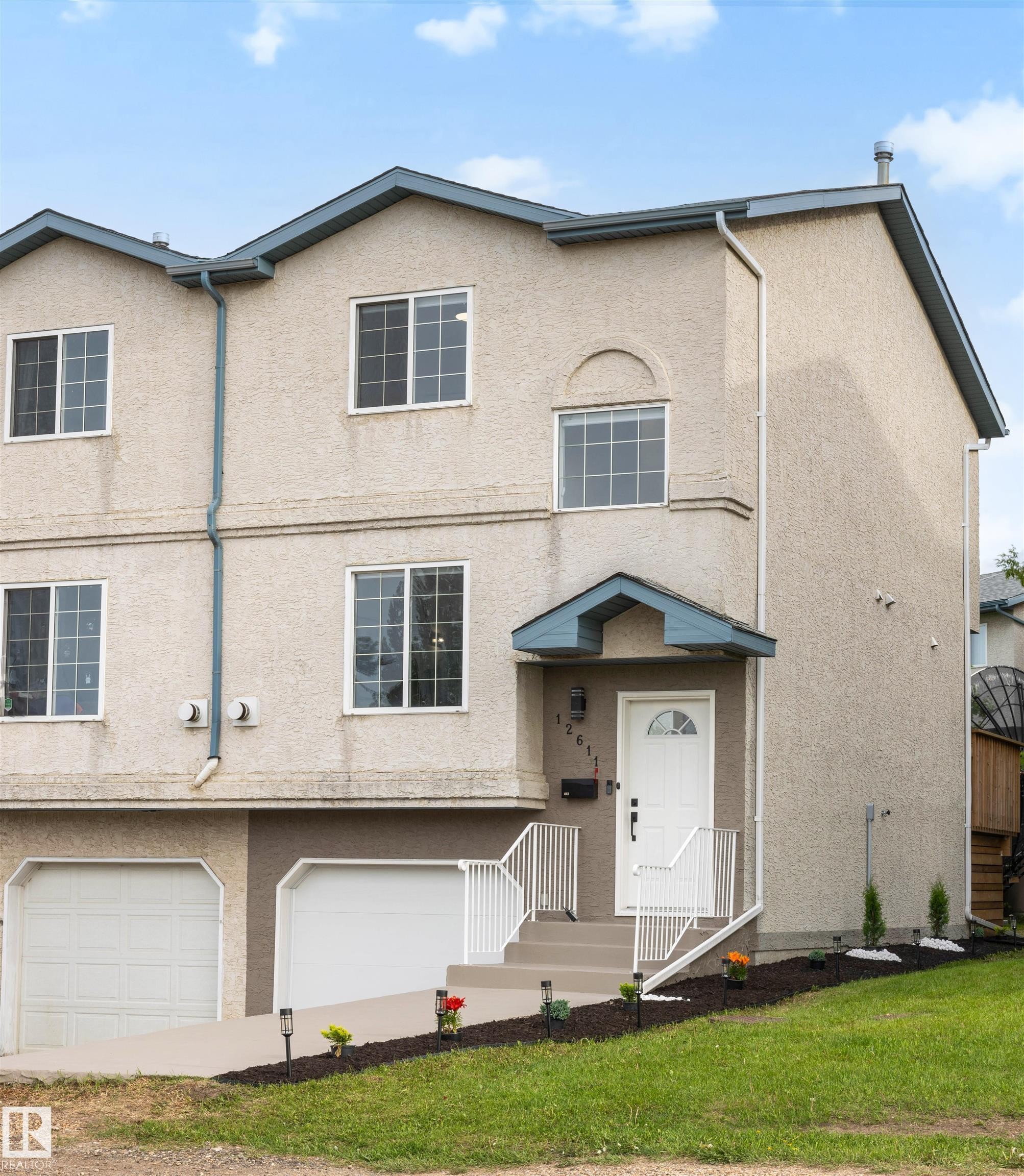 Multi-level stucco exterior featuring an integrated garage, covered front entry, and multiple windows - 12611 47 Street, Edmonton, AB