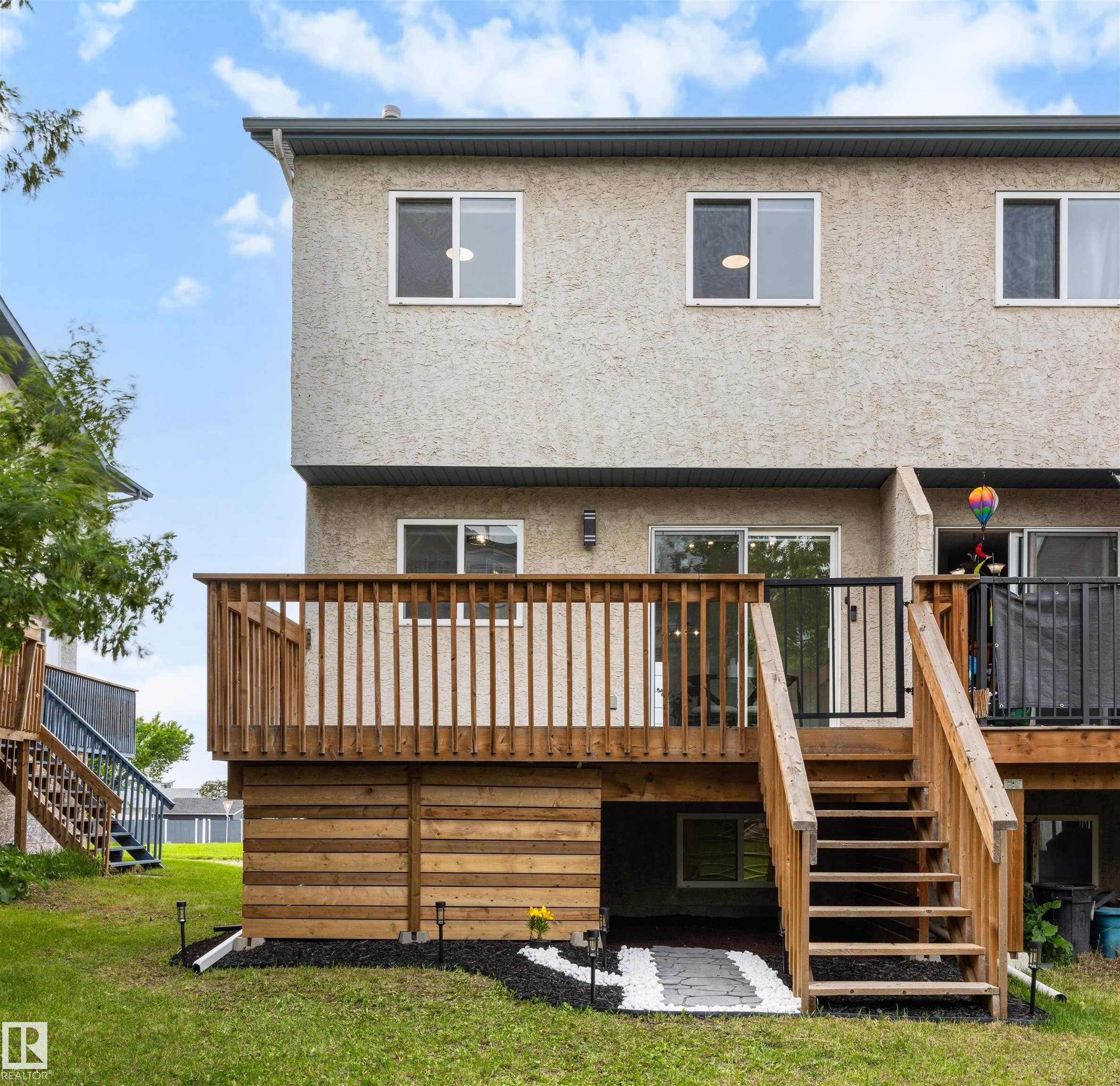 Rear exterior featuring a spacious wood deck with stairs to the yard, a stucco facade, and multiple windows - 12611 47 Street, Edmonton, AB
