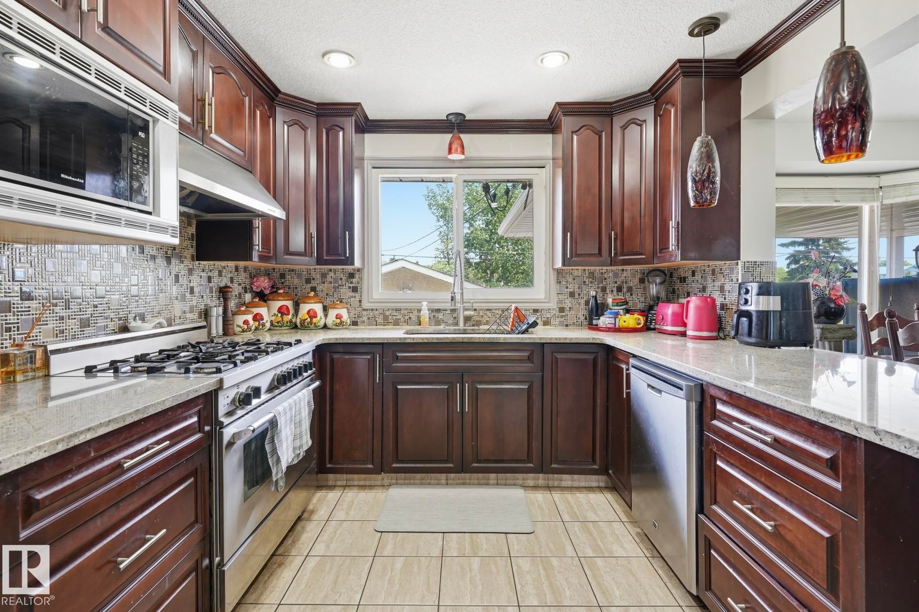 U-shaped kitchen featuring wood cabinetry, light-toned granite countertops, and a mosaic tile backsplash - 12131 101 Street Nw, Edmonton, AB