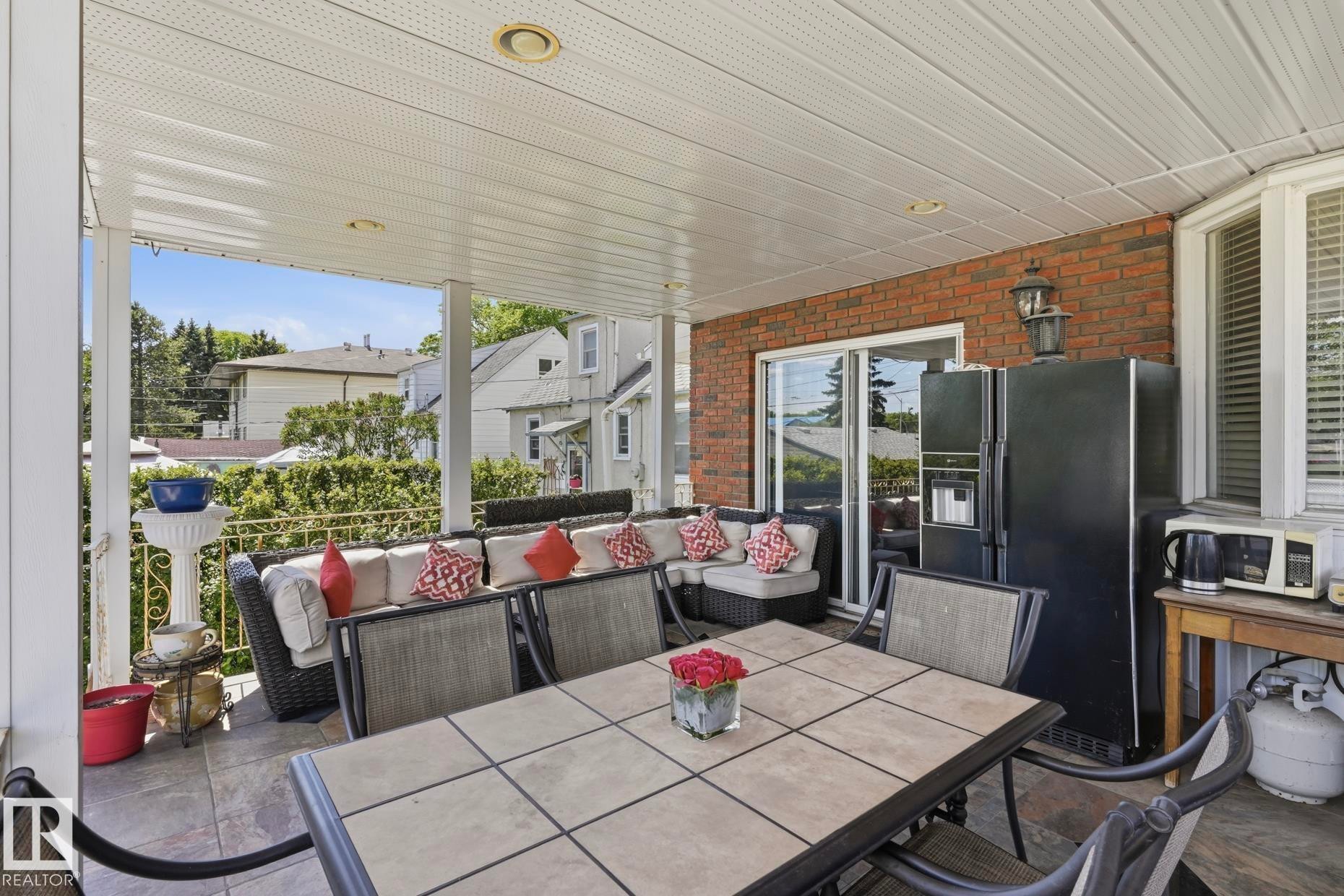 Covered patio featuring a paneled ceiling with recessed lighting, brick exterior wall, and sliding glass door - 12131 101 Street Nw, Edmonton, AB