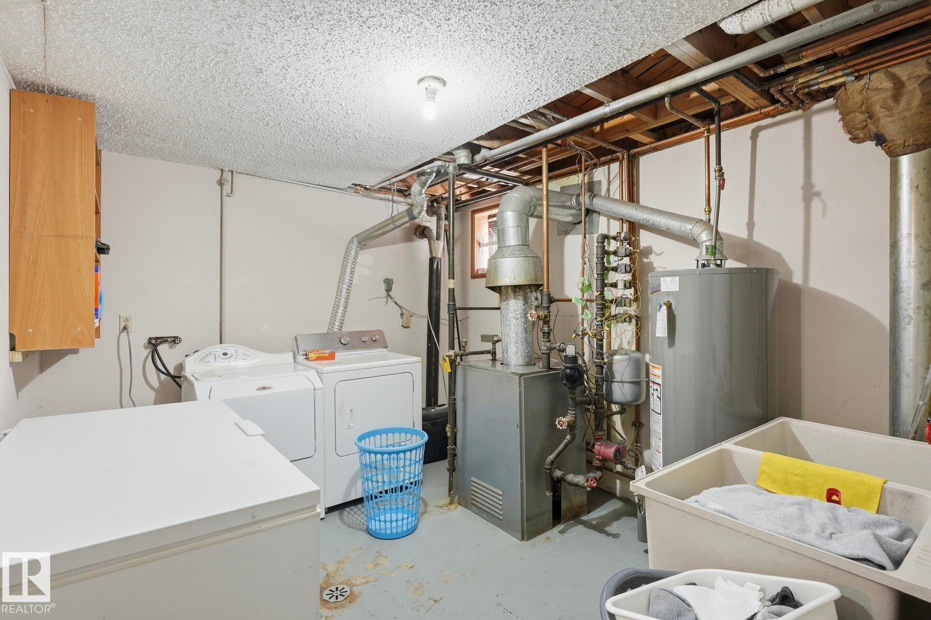 Utility area featuring a laundry sink, exposed overhead piping, and a water heater - 12131 101 Street Nw, Edmonton, AB