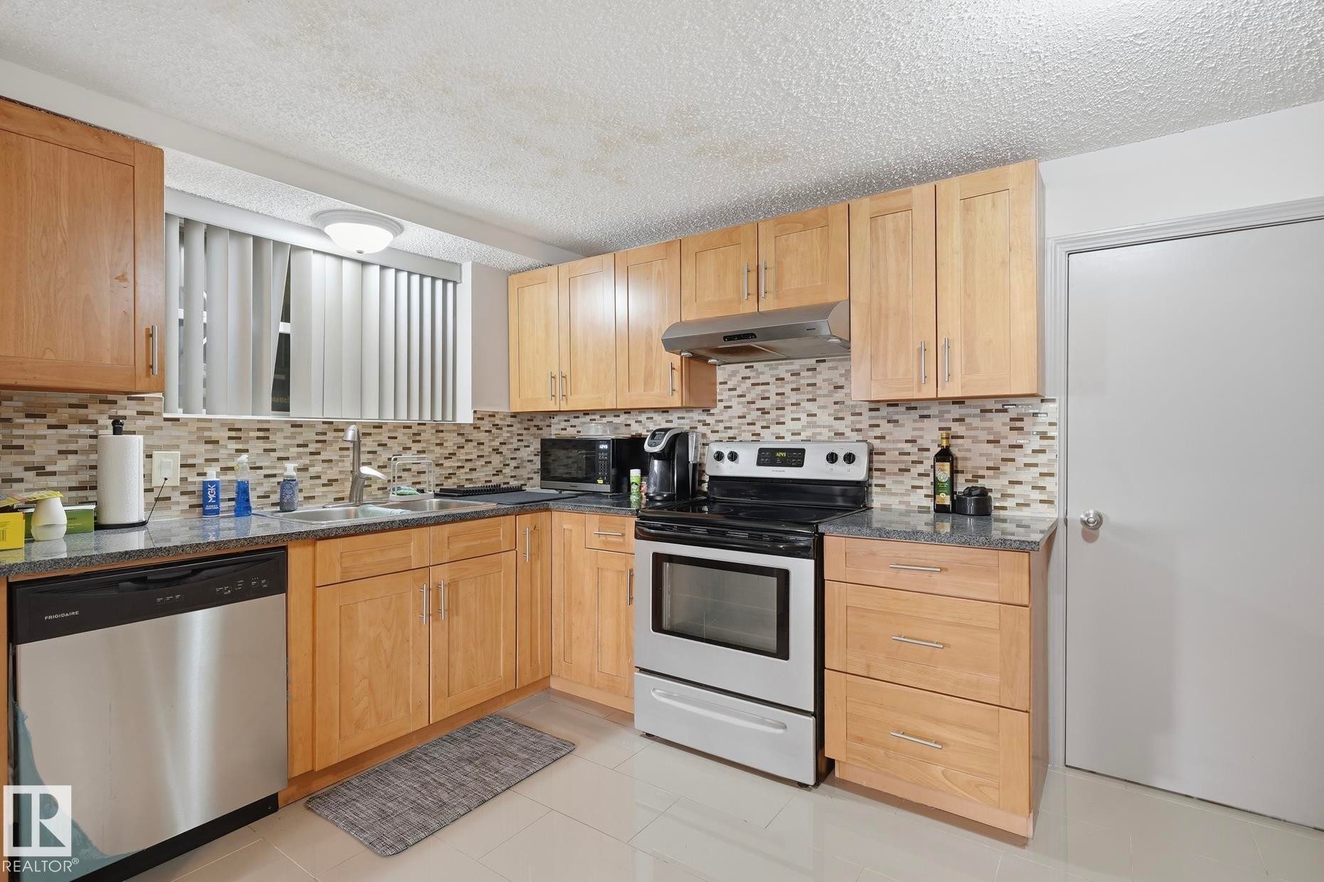 Kitchen featuring wood-finish cabinetry, granite-style countertops, and a mosaic tile backsplash - 12131 101 Street Nw, Edmonton, AB