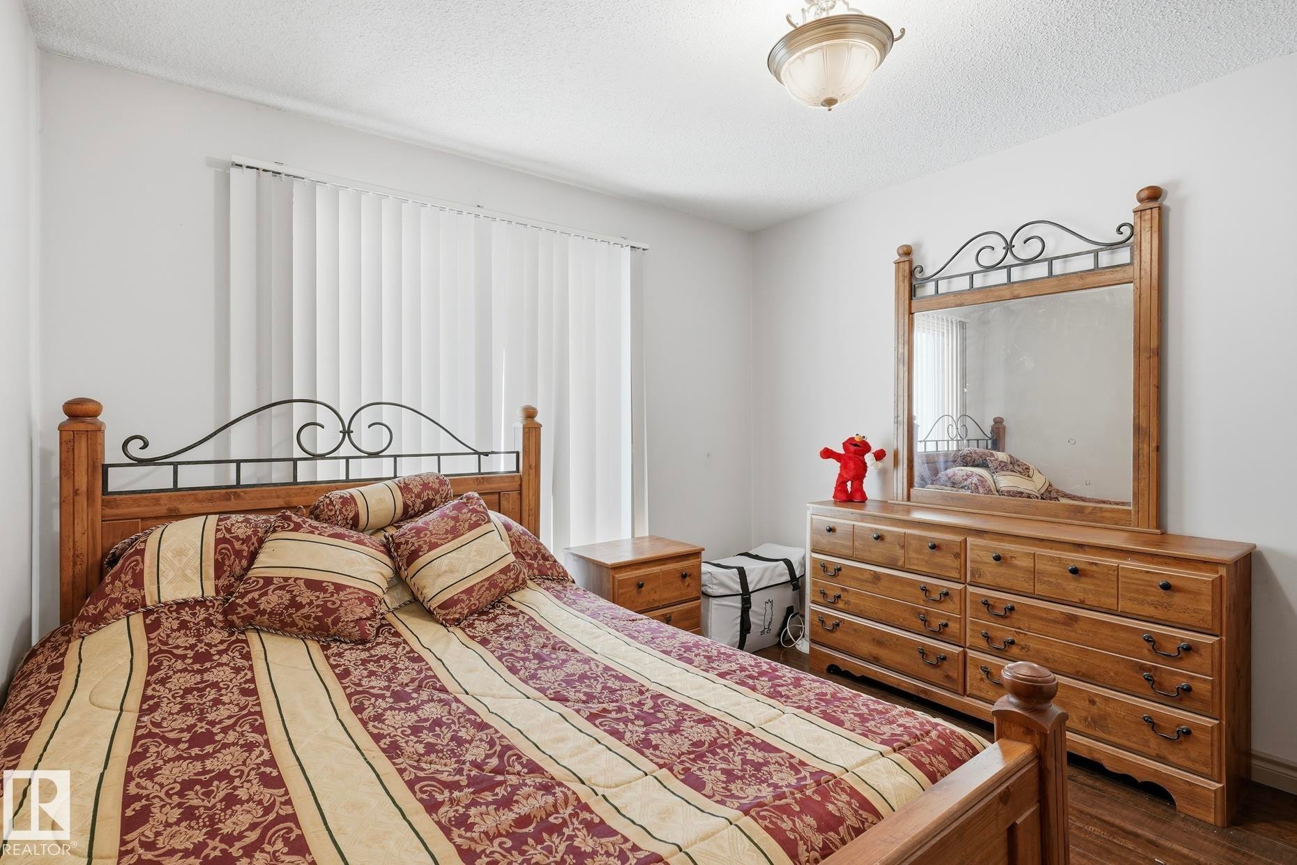 Bedroom featuring wood-finish flooring, a ceiling-mounted light fixture, and vertical blinds - 12131 101 Street Nw, Edmonton, AB