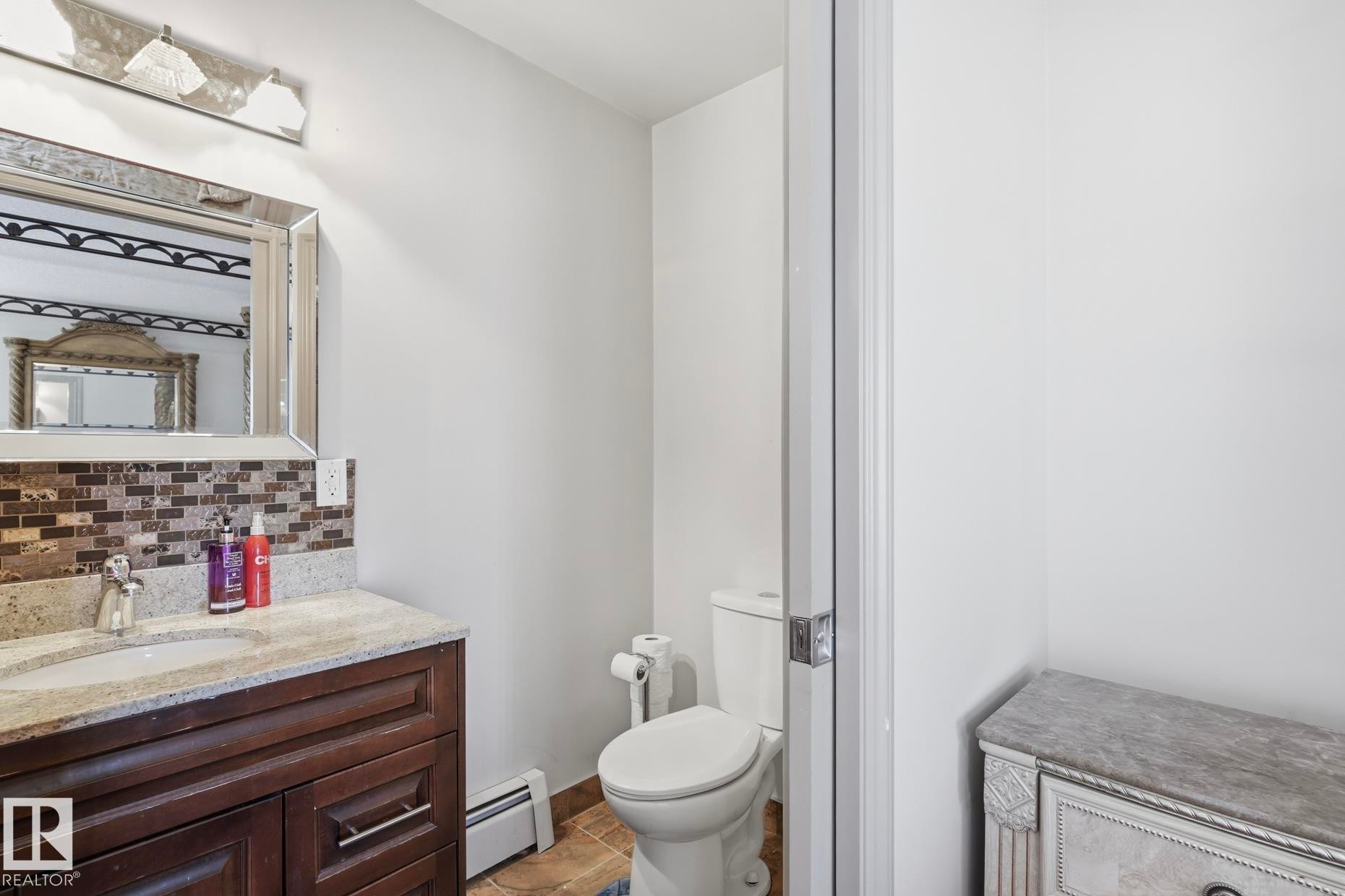 Bathroom with a dark wood-finish vanity, light-toned countertop, and brown mosaic tile backsplash - 12131 101 Street Nw, Edmonton, AB
