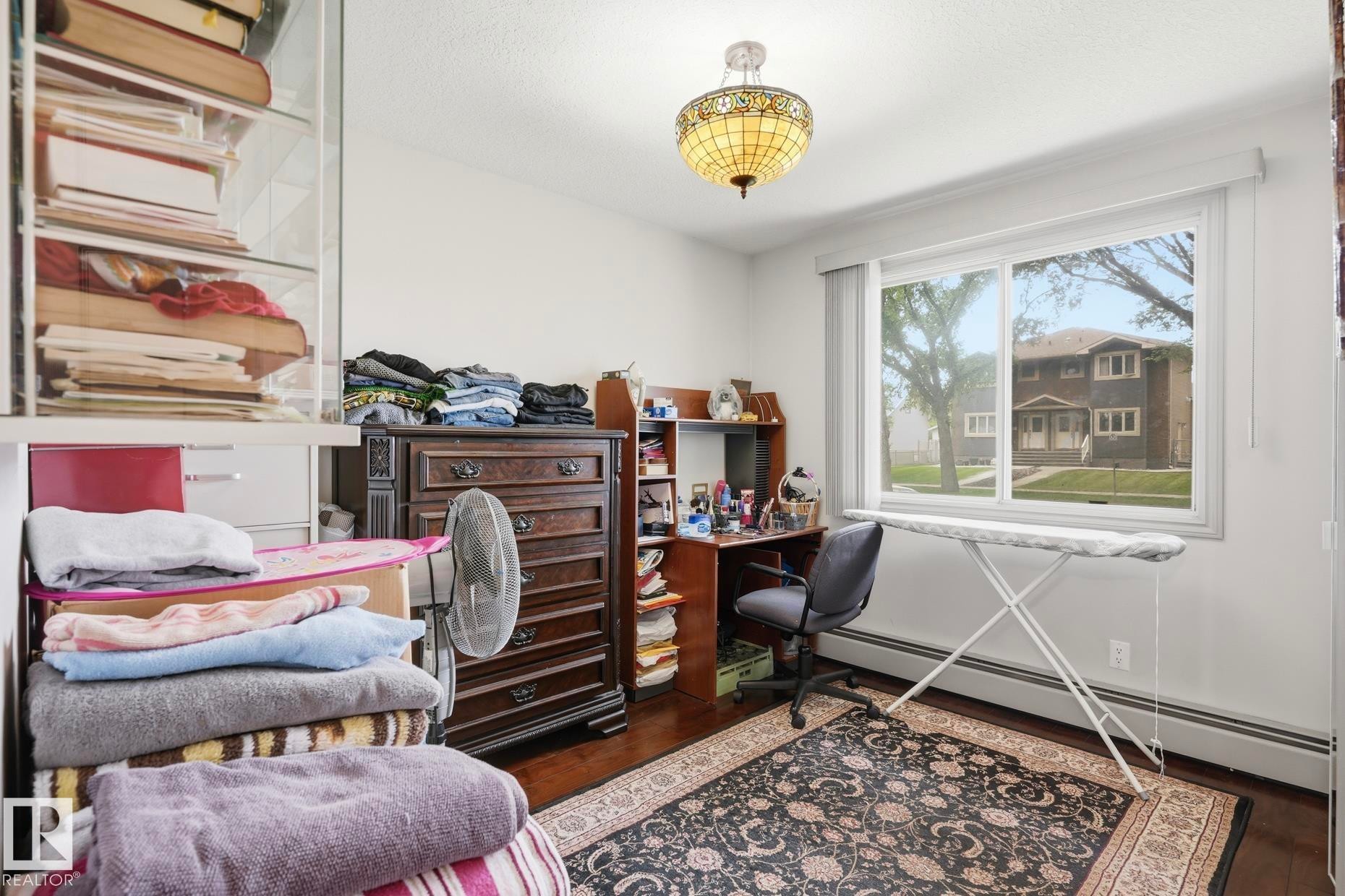 Bright room featuring a large window, dark wood-finish flooring, and a decorative ceiling light fixture - 12131 101 Street Nw, Edmonton, AB