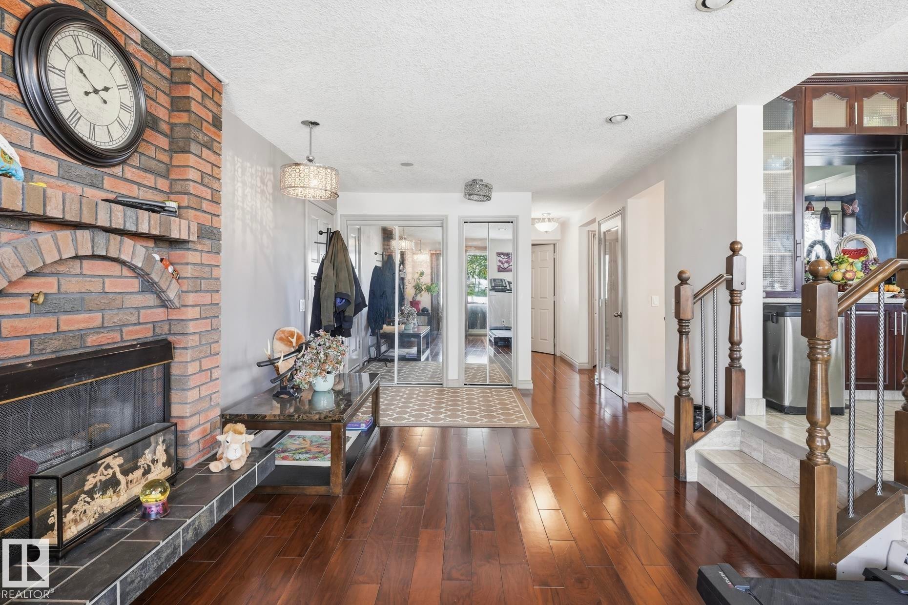 Brick fireplace with tile hearth, wood-finish flooring, mirrored closet doors, and hardwood staircase - 12131 101 Street Nw, Edmonton, AB