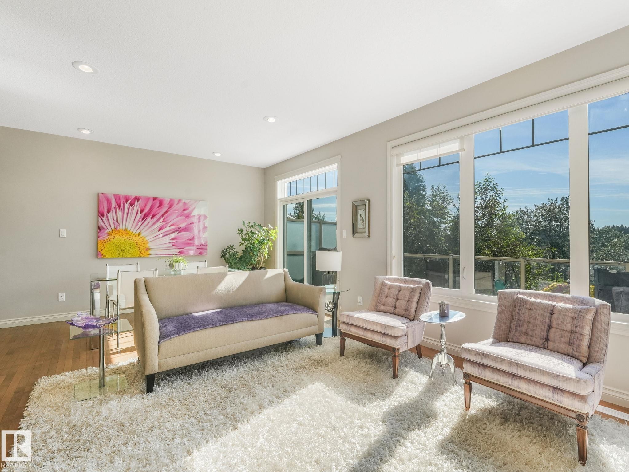Spacious living area featuring large windows, recessed ceiling lighting, light wood-finish flooring, and a glass-paneled balcony - 3 1641 James Mowatt Trail, Edmonton, AB
