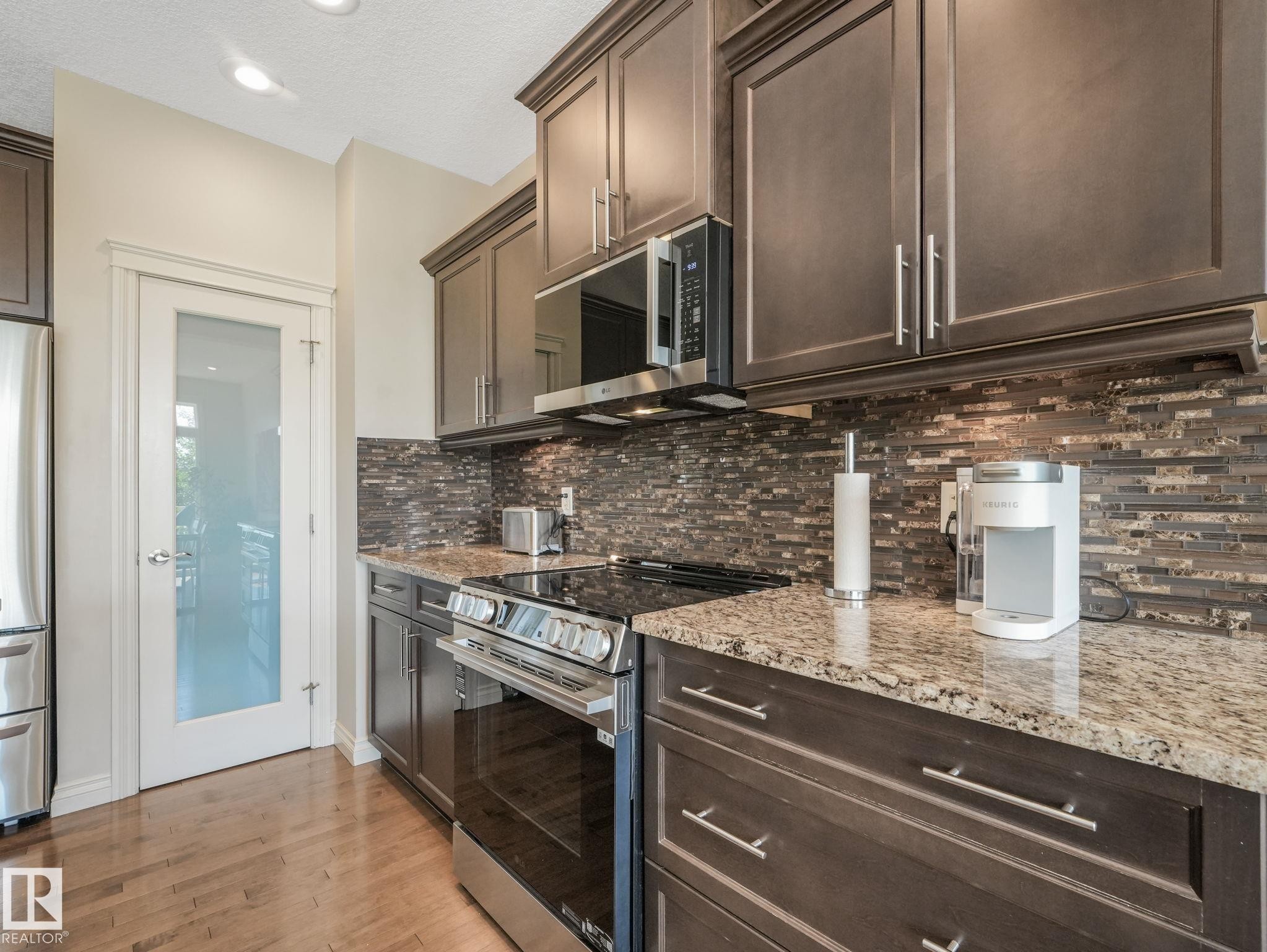 Kitchen featuring wood-finish flooring, granite countertops, an undermount sink, and dark wood cabinetry - 3 1641 James Mowatt Trail, Edmonton, AB
