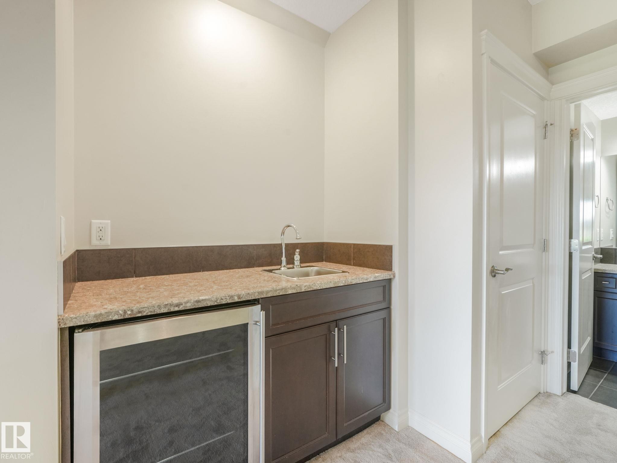 Wet bar featuring a stainless steel beverage refrigerator, compact sink, granite-style countertop, and dark wood-finish cabinetry - 3 1641 James Mowatt Trail, Edmonton, AB