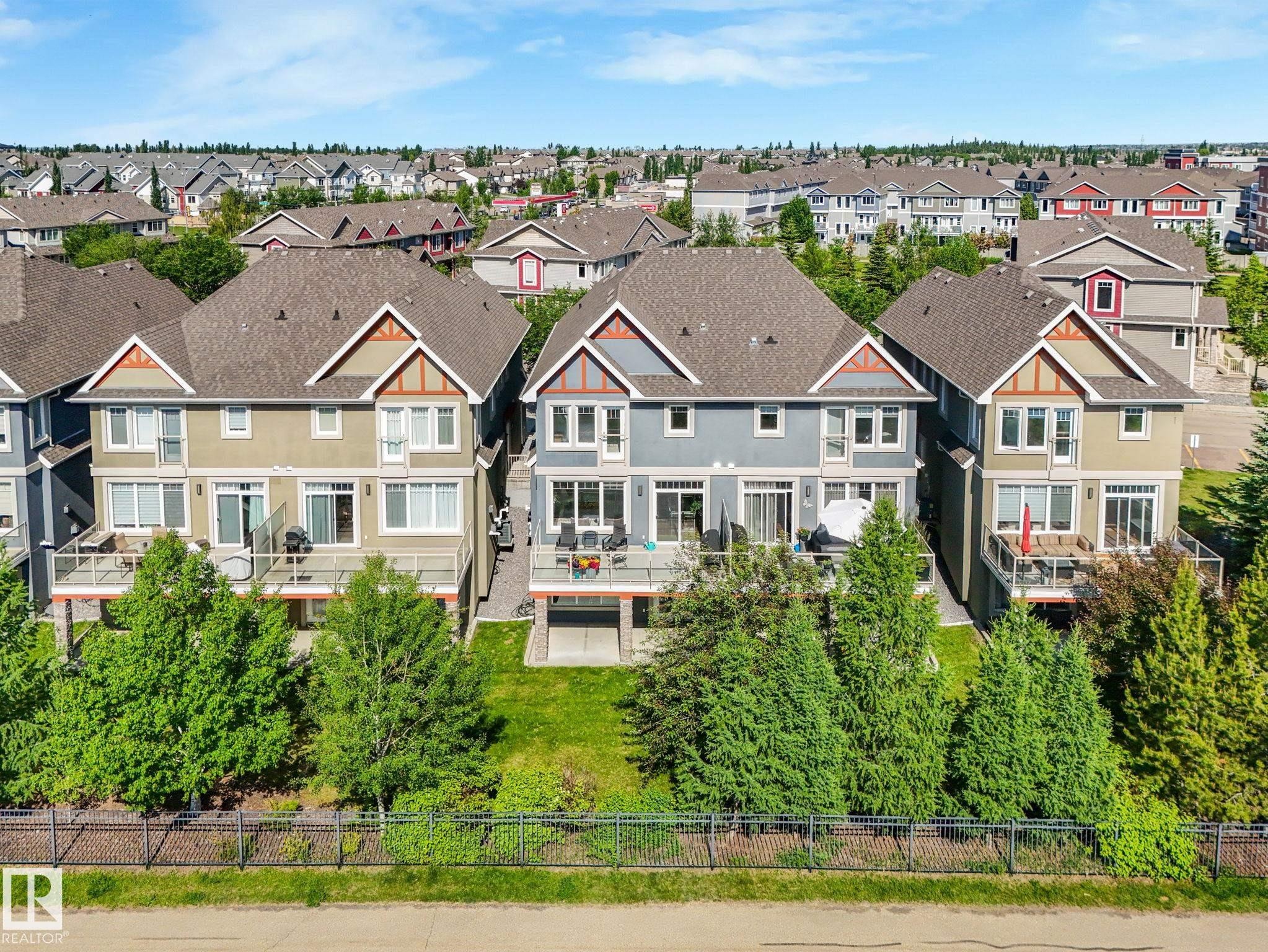 Rear exteriors of three multi-story properties featuring individual decks, sliding glass doors, and ground-level patios - 3 1641 James Mowatt Trail, Edmonton, AB