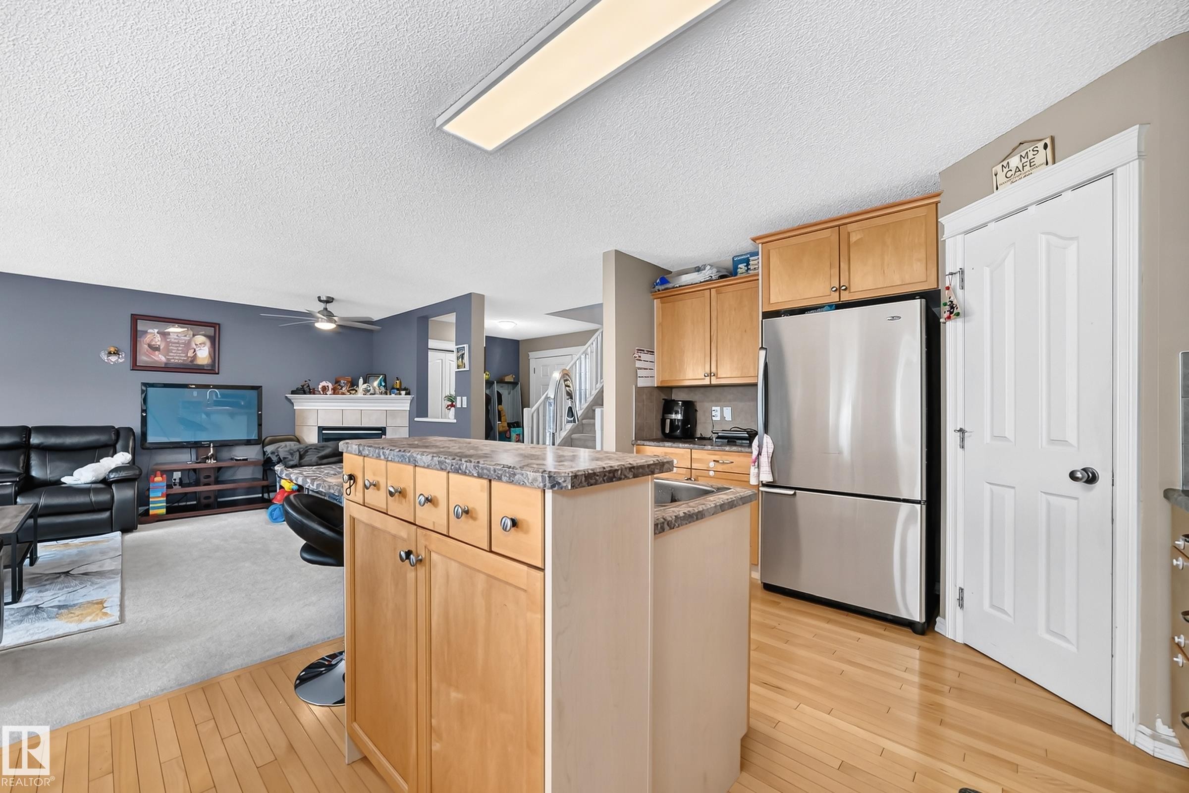 Kitchen featuring wood-finish flooring, light wood cabinetry, stainless steel refrigerator, and a kitchen island with a stone-finish countertop - 3224 26 Street, Edmonton, AB