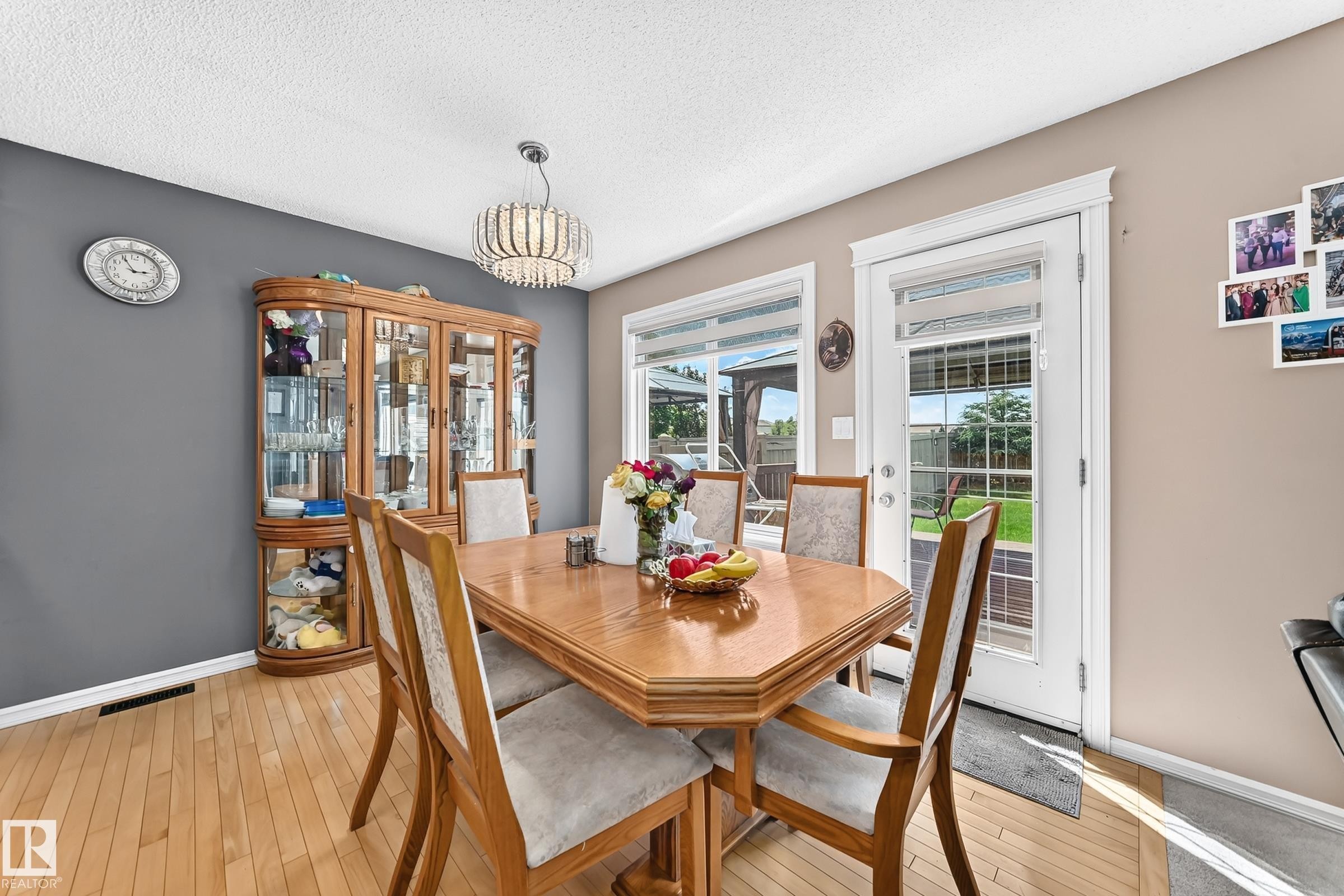 Dining area featuring light wood-finish flooring, a contemporary chandelier, and direct access to the exterior through a glass-paneled door - 3224 26 Street, Edmonton, AB