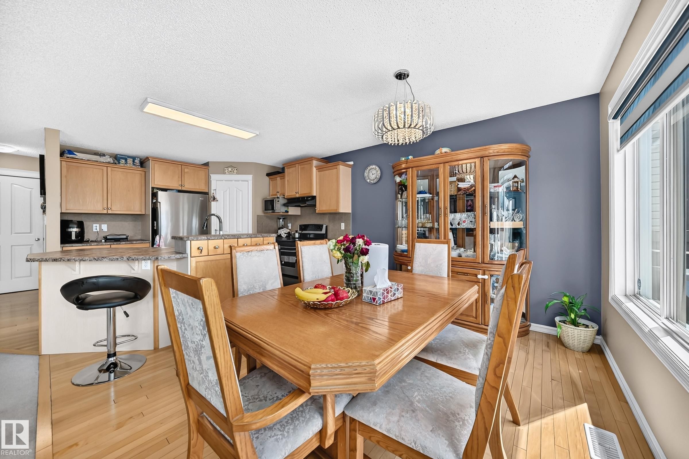 Open-concept dining area featuring wood-finish flooring, a contemporary chandelier, and a built-in display cabinet - 3224 26 Street, Edmonton, AB