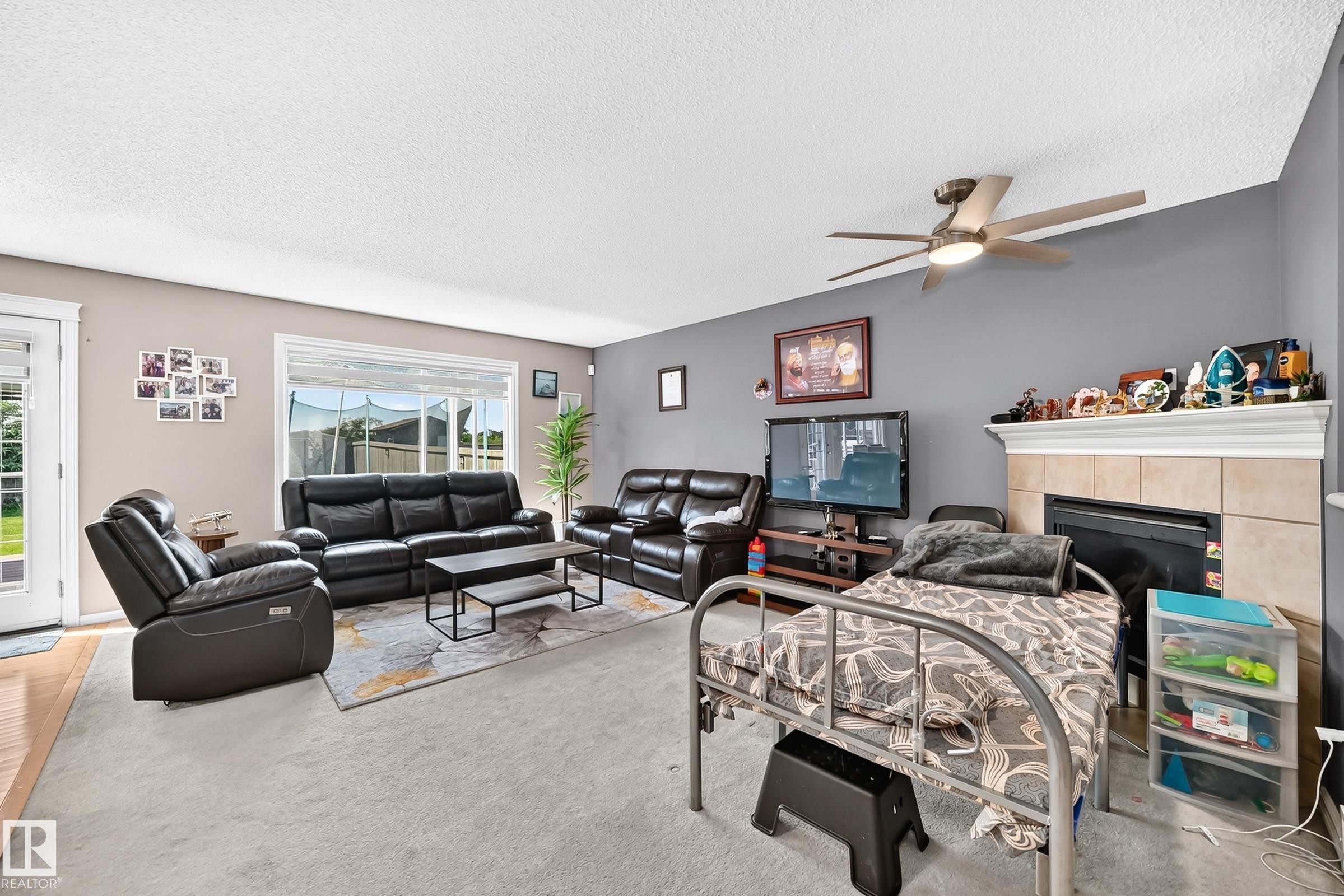 Living area featuring a ceiling fan, fireplace with tile surround, and large window - 3224 26 Street, Edmonton, AB