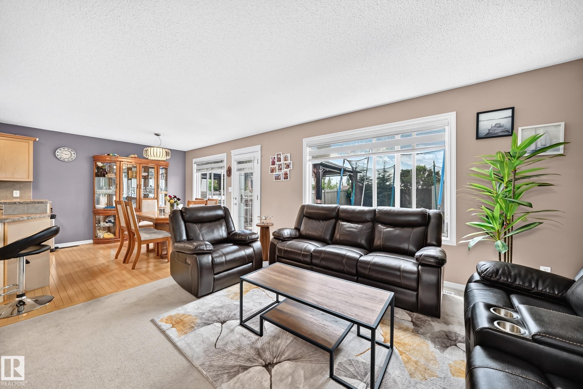 Open-concept living space featuring a window with white trim, light-colored carpeting, and a dining area with wood-finish flooring - 3224 26 Street, Edmonton, AB