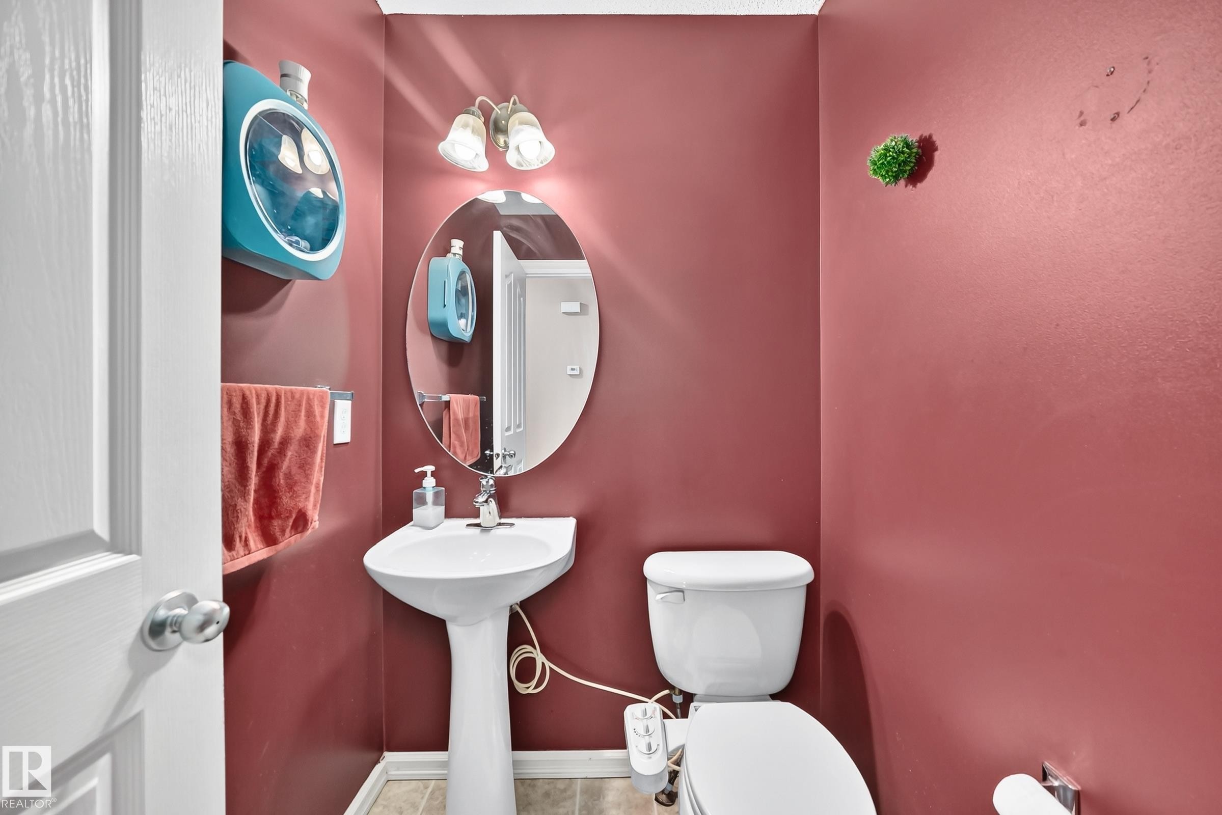 Pedestal sink with an oval frameless mirror, complemented by a two-light vanity fixture - 3224 26 Street, Edmonton, AB