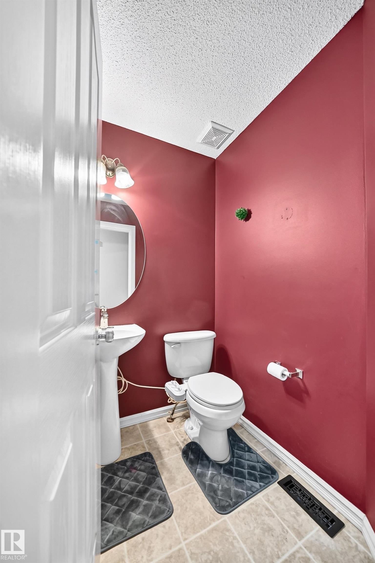 Compact powder room featuring a pedestal sink, round mirror, and tile flooring - 3224 26 Street, Edmonton, AB