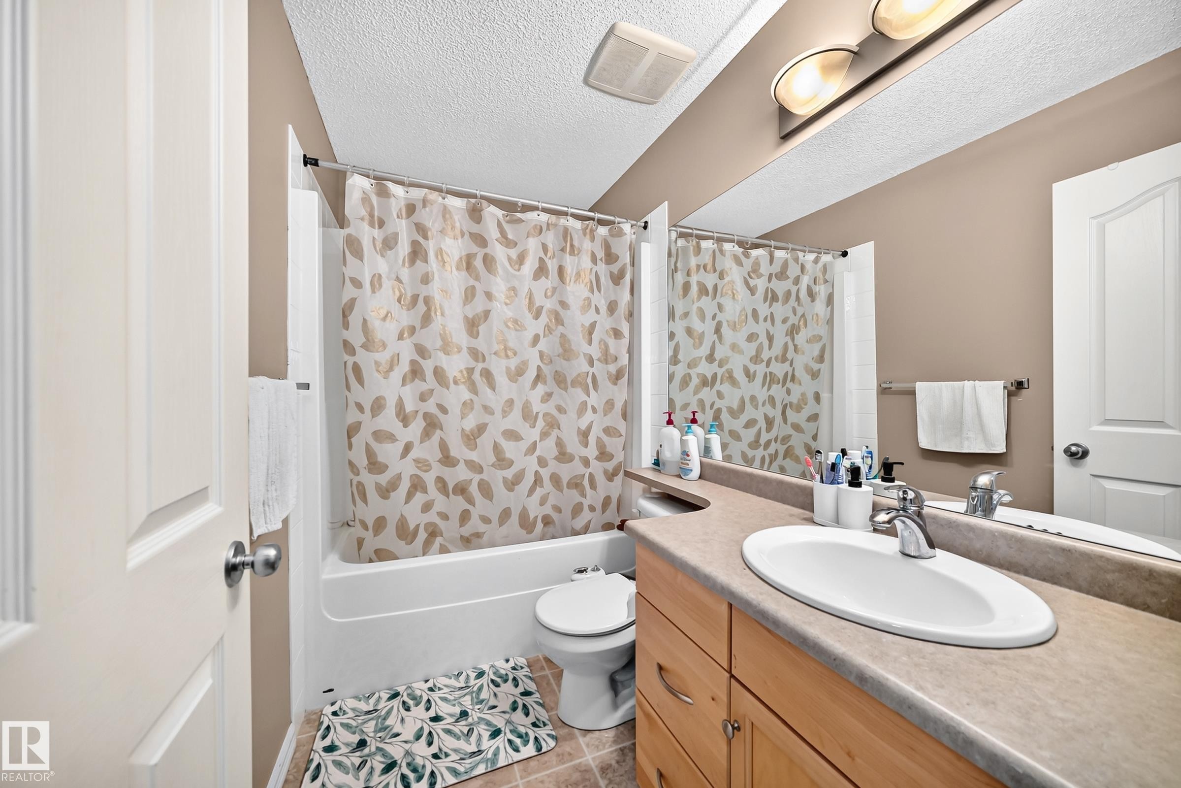 Bathroom featuring a shower-tub combination, wood-finish vanity with a single sink, large wall-mounted mirror, and tile flooring - 3224 26 Street, Edmonton, AB