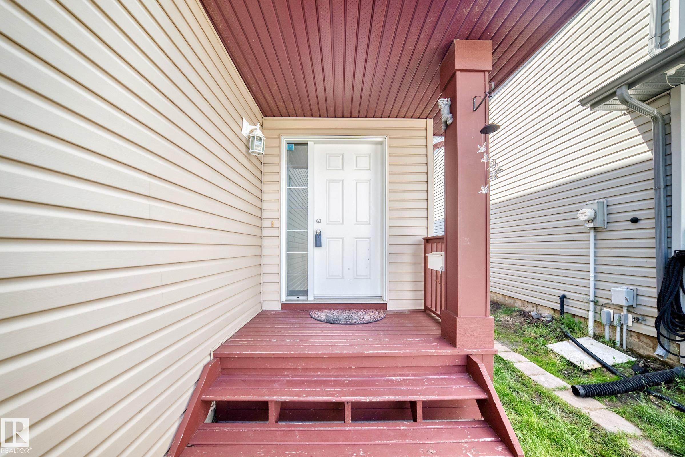 Welcoming entry with a white paneled door and sidelight, complemented by a red-stained wood porch and matching steps - 3224 26 Street, Edmonton, AB