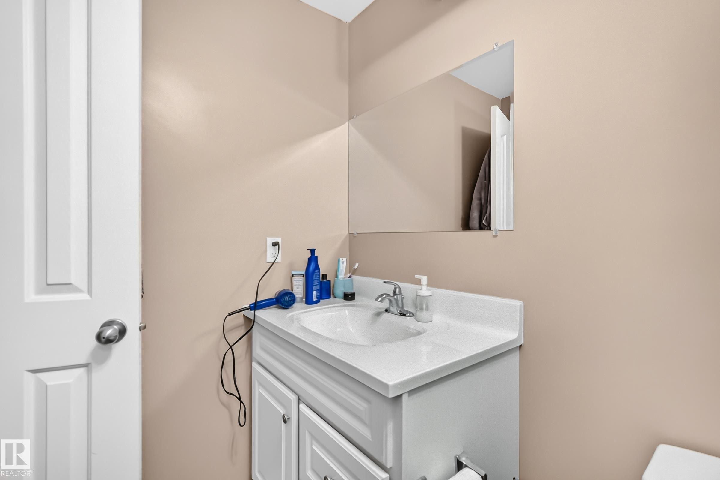 Built-in vanity with a white countertop and integrated sink, chrome faucet, and rectangular wall mirror - 3224 26 Street, Edmonton, AB