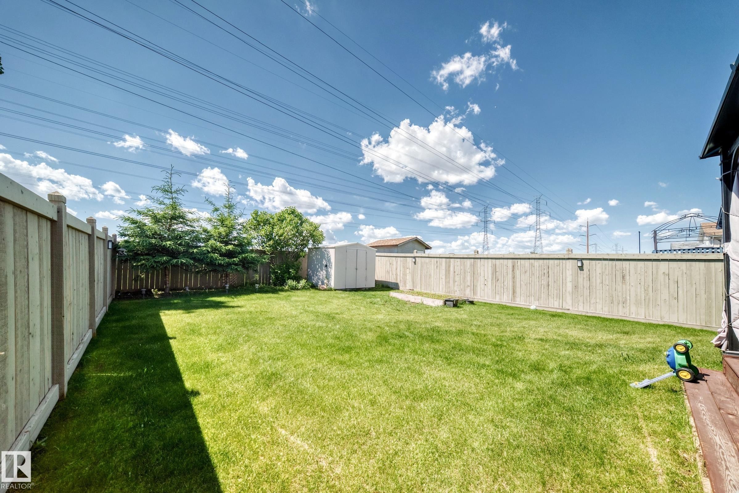 Expansive backyard featuring a large green lawn, full privacy fencing, mature trees, and a storage shed - 3224 26 Street, Edmonton, AB