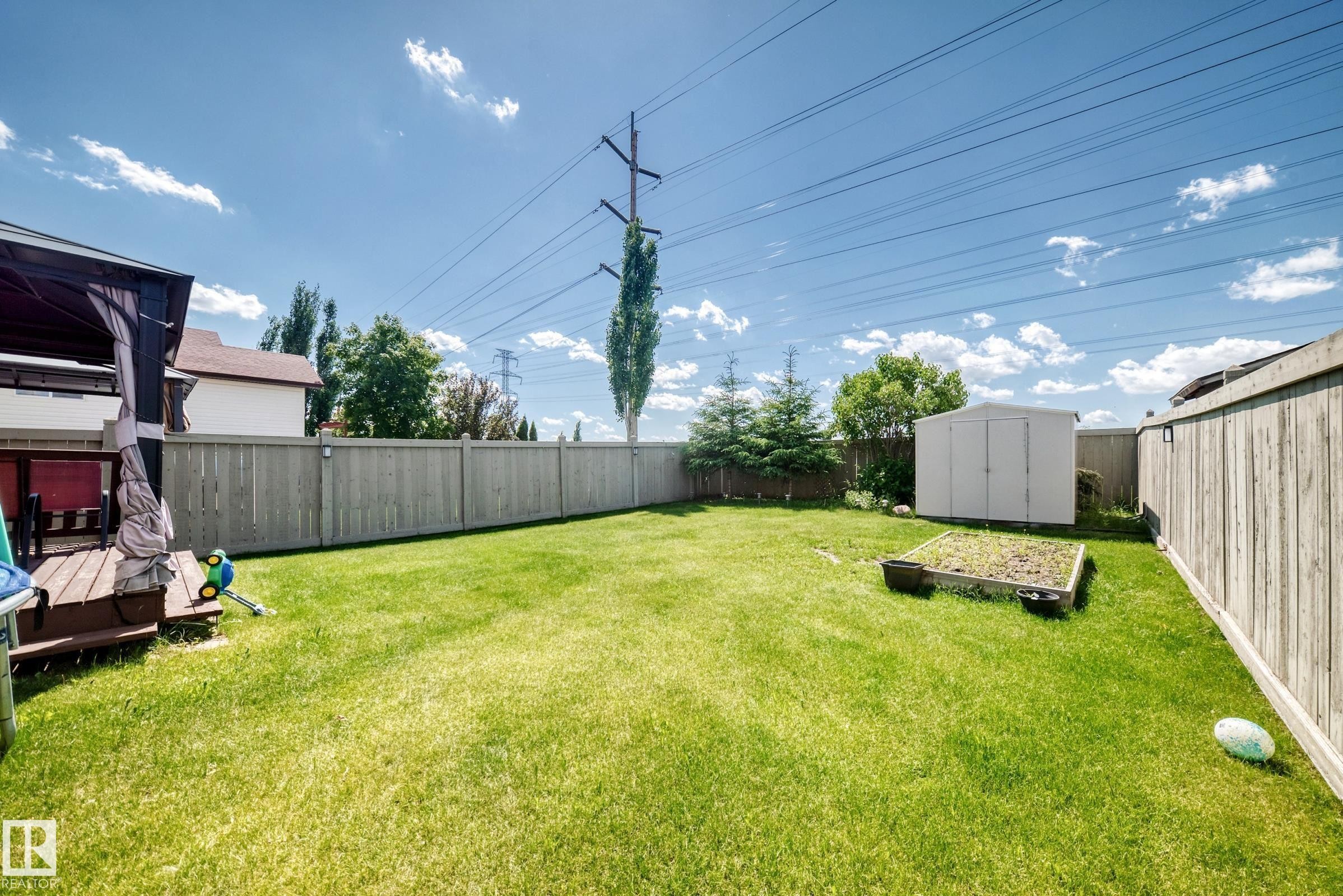 Expansive fenced backyard featuring a substantial lawn area, a functional storage shed, and a raised garden bed - 3224 26 Street, Edmonton, AB