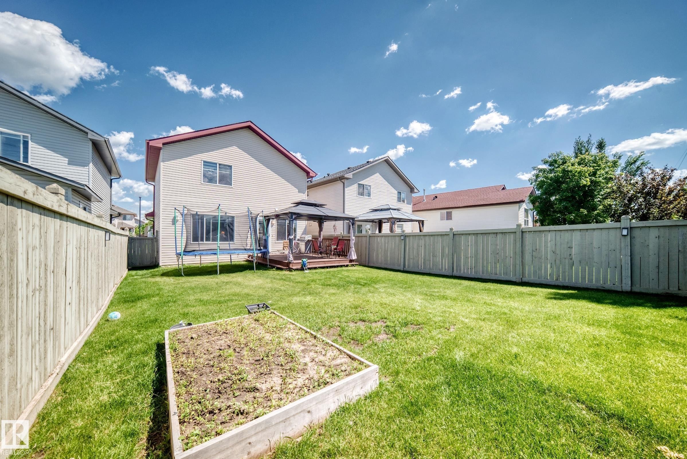 Expansive fenced backyard featuring a wood deck, sheltered gazebo, and a raised garden bed - 3224 26 Street, Edmonton, AB