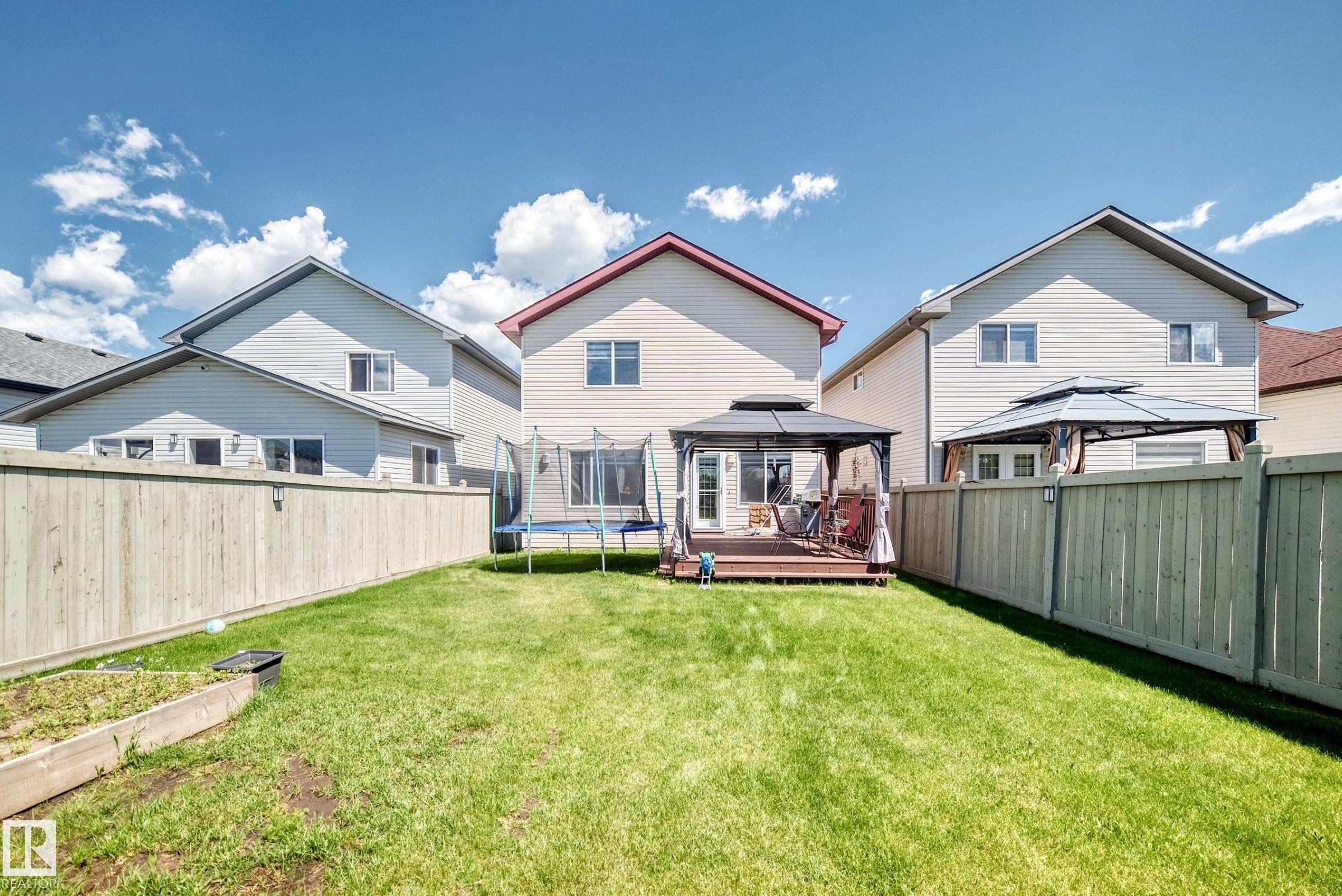 Expansive fenced backyard featuring a grassy lawn, a wooden deck, and a covered gazebo - 3224 26 Street, Edmonton, AB