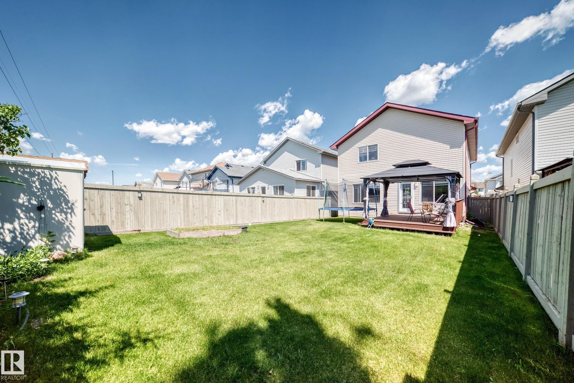Expansive backyard featuring a manicured lawn, full privacy fencing, and a dedicated patio space with a gazebo - 3224 26 Street, Edmonton, AB