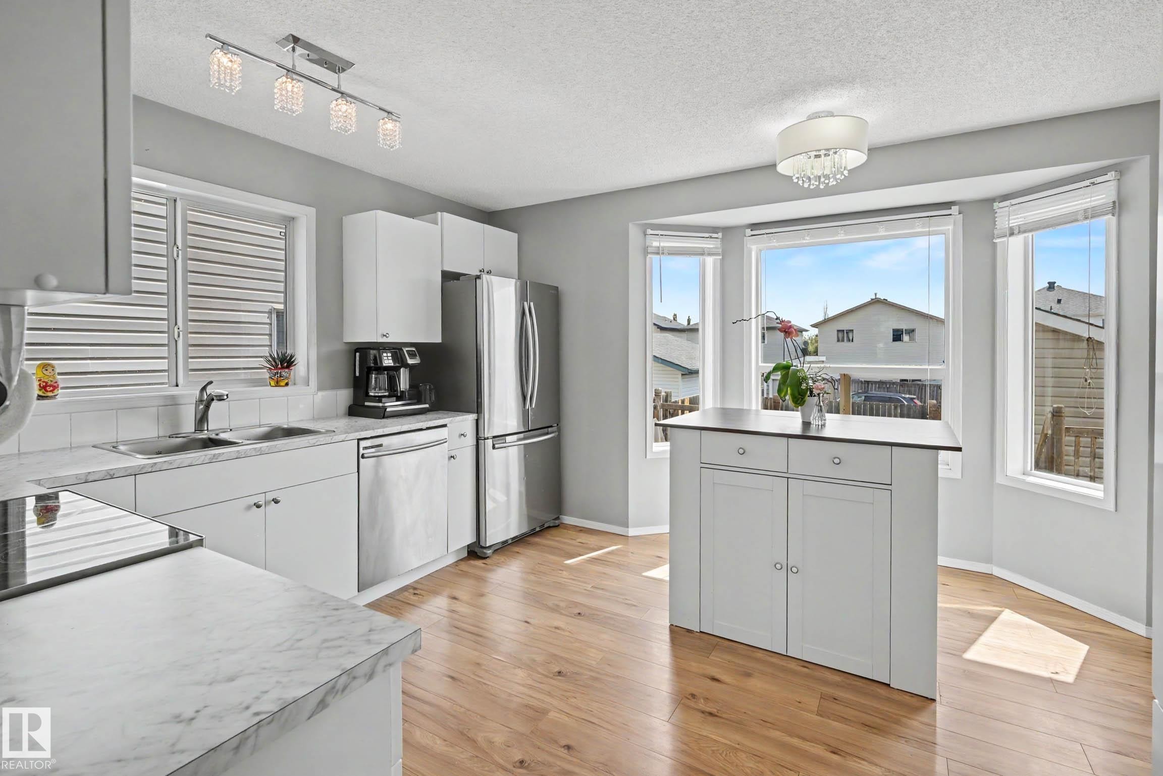 Bright kitchen featuring wood-finish flooring and white cabinetry - 2123 36 Avenue, Edmonton, AB - Indoor Photo Showing Kitchen With Stainless Steel Kitchen With Double Sink