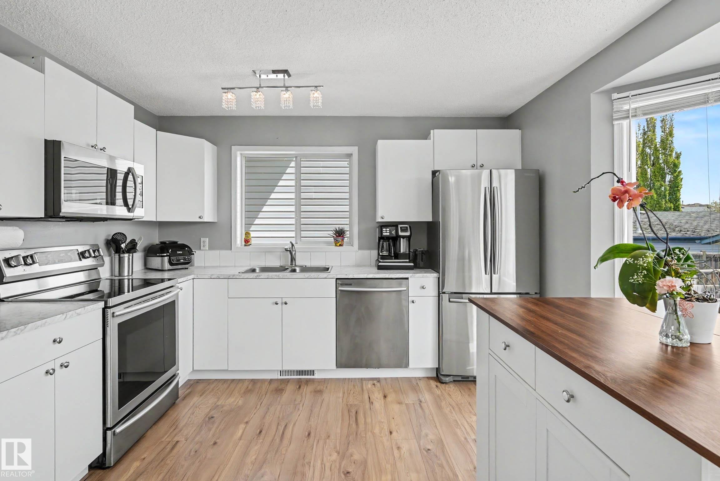Modern kitchen featuring white cabinetry, wood-finish flooring, and stainless steel appliances - 2123 36 Avenue, Edmonton, AB - Indoor Photo Showing Kitchen With Stainless Steel Kitchen With Double Sink