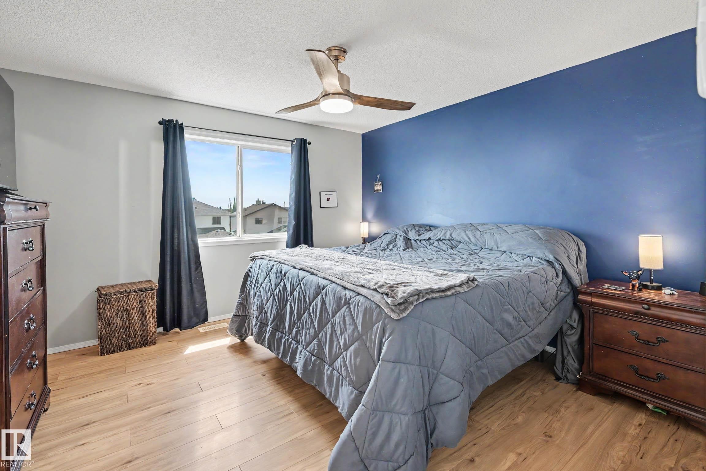 Spacious room featuring wood-finish flooring, a contemporary ceiling fan with integrated lighting, and a prominent accent wall - 2123 36 Avenue, Edmonton, AB - Indoor Photo Showing Bedroom