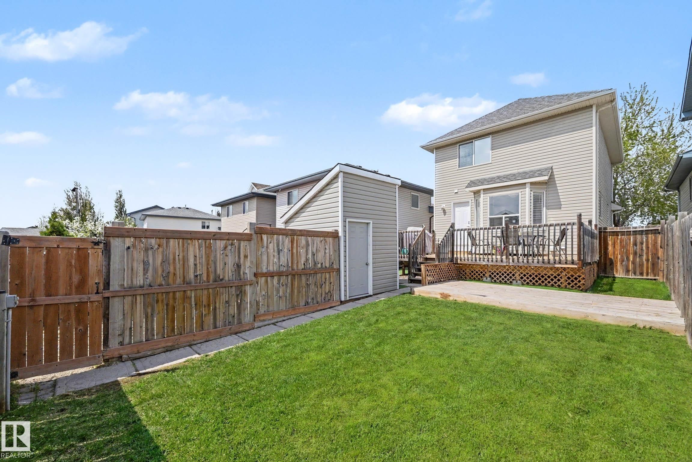 Expansive backyard featuring a manicured lawn, a concrete patio area, and a private wood deck with lattice skirting - 2123 36 Avenue, Edmonton, AB - Outdoor With Deck Patio Veranda With Exterior