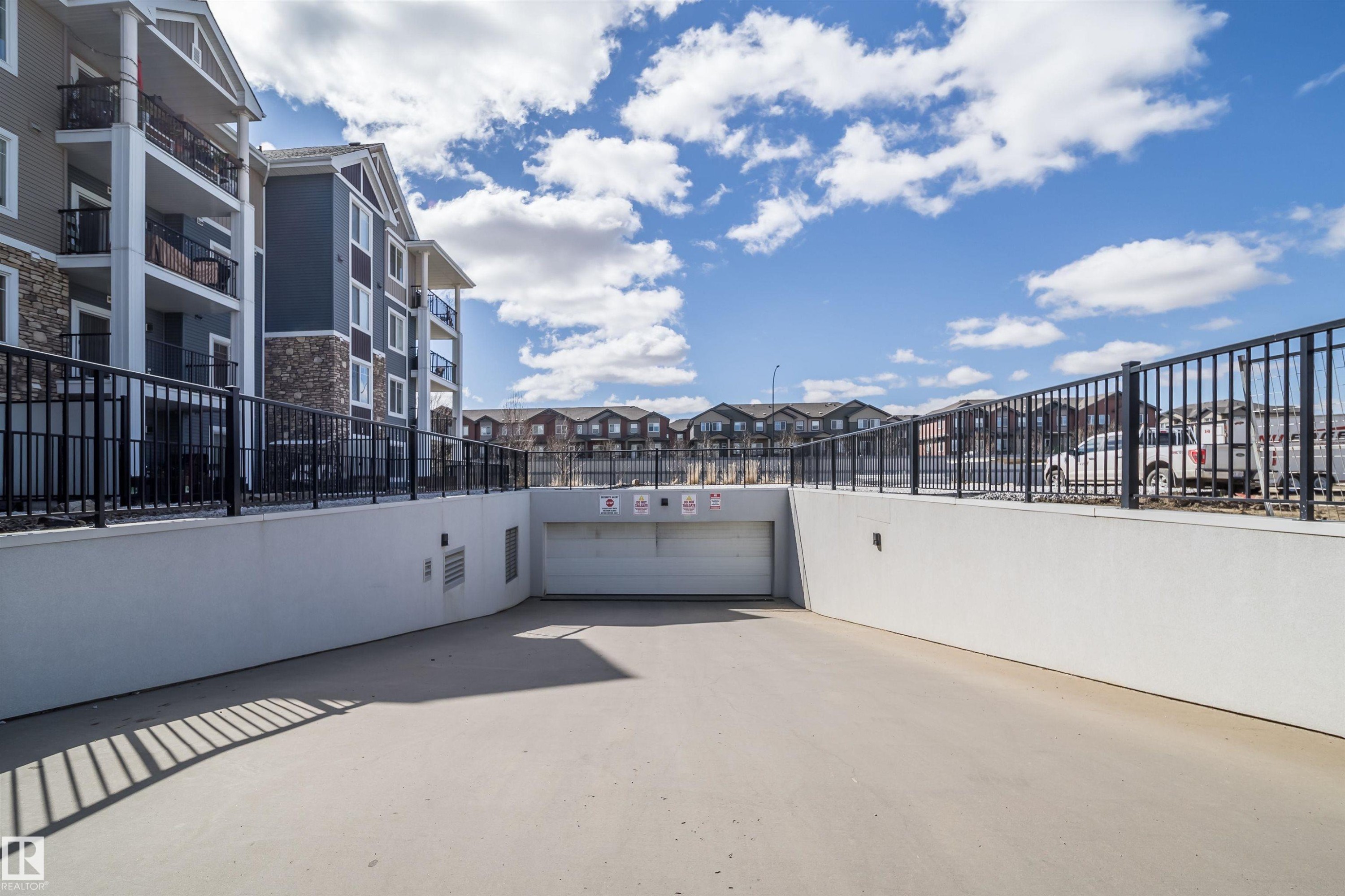 Concrete ramp leading to an underground garage with a white garage door - 421 4008 Savaryn Drive, Edmonton, AB - Outdoor