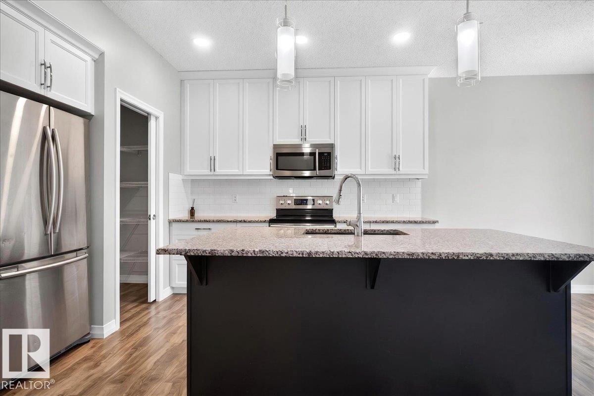 Modern kitchen featuring a dark island with an undermount sink and gooseneck faucet - 17203 71 Street, Edmonton, AB