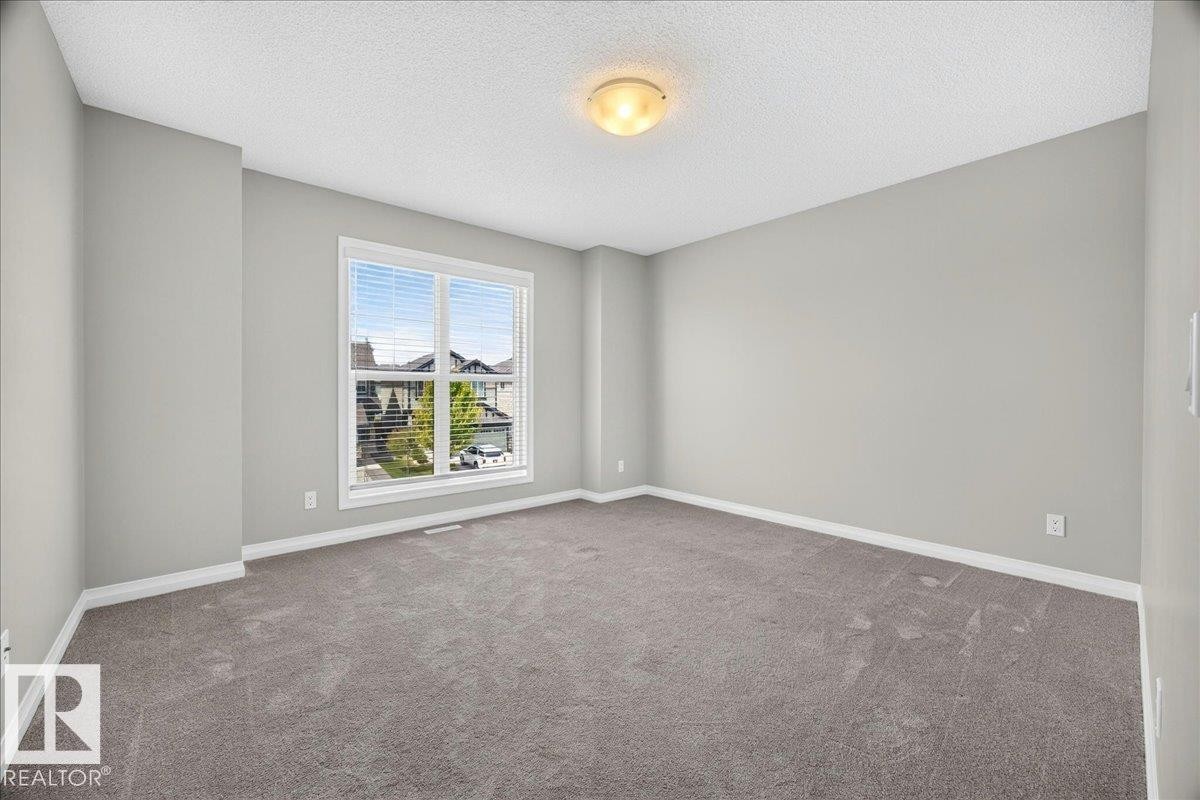 Spacious room featuring a large window with horizontal blinds, neutral-toned walls, gray carpeting, and white baseboards - 17203 71 Street, Edmonton, AB