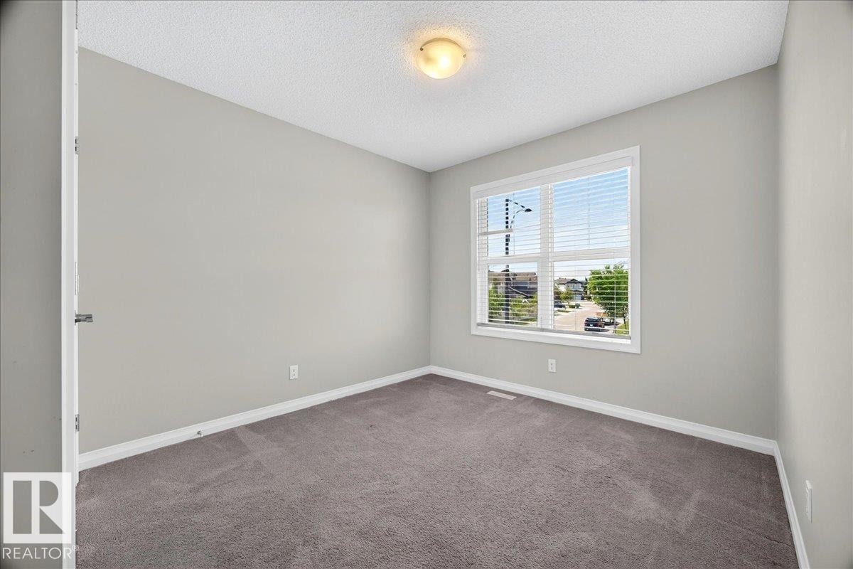 Bright room featuring a large window with white blinds, neutral gray walls, and gray carpeting - 17203 71 Street, Edmonton, AB