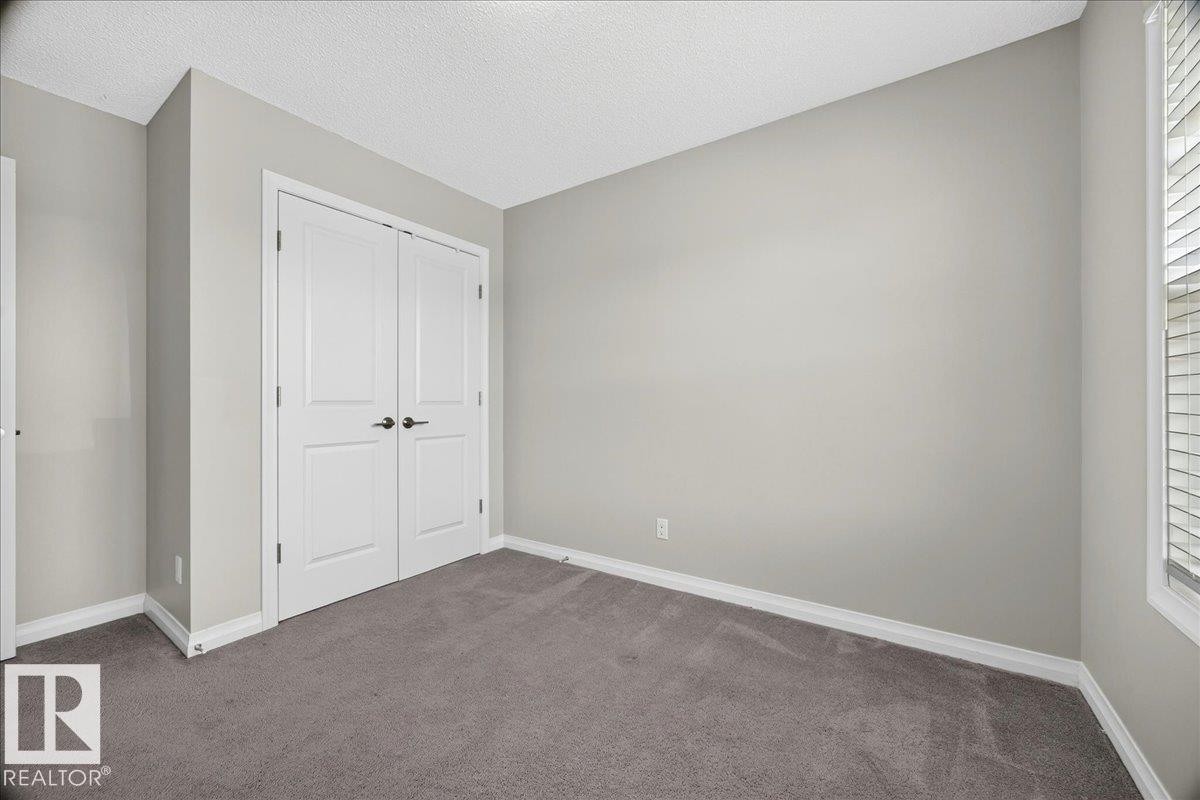 Spacious room featuring neutral painted walls, gray carpet flooring, white baseboards, and a double-door closet with dark hardware - 17203 71 Street, Edmonton, AB