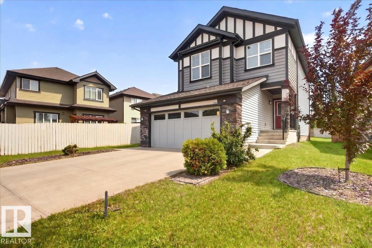 Two-story residence featuring a two-car garage, concrete driveway, and a red front door - 17203 71 Street, Edmonton, AB