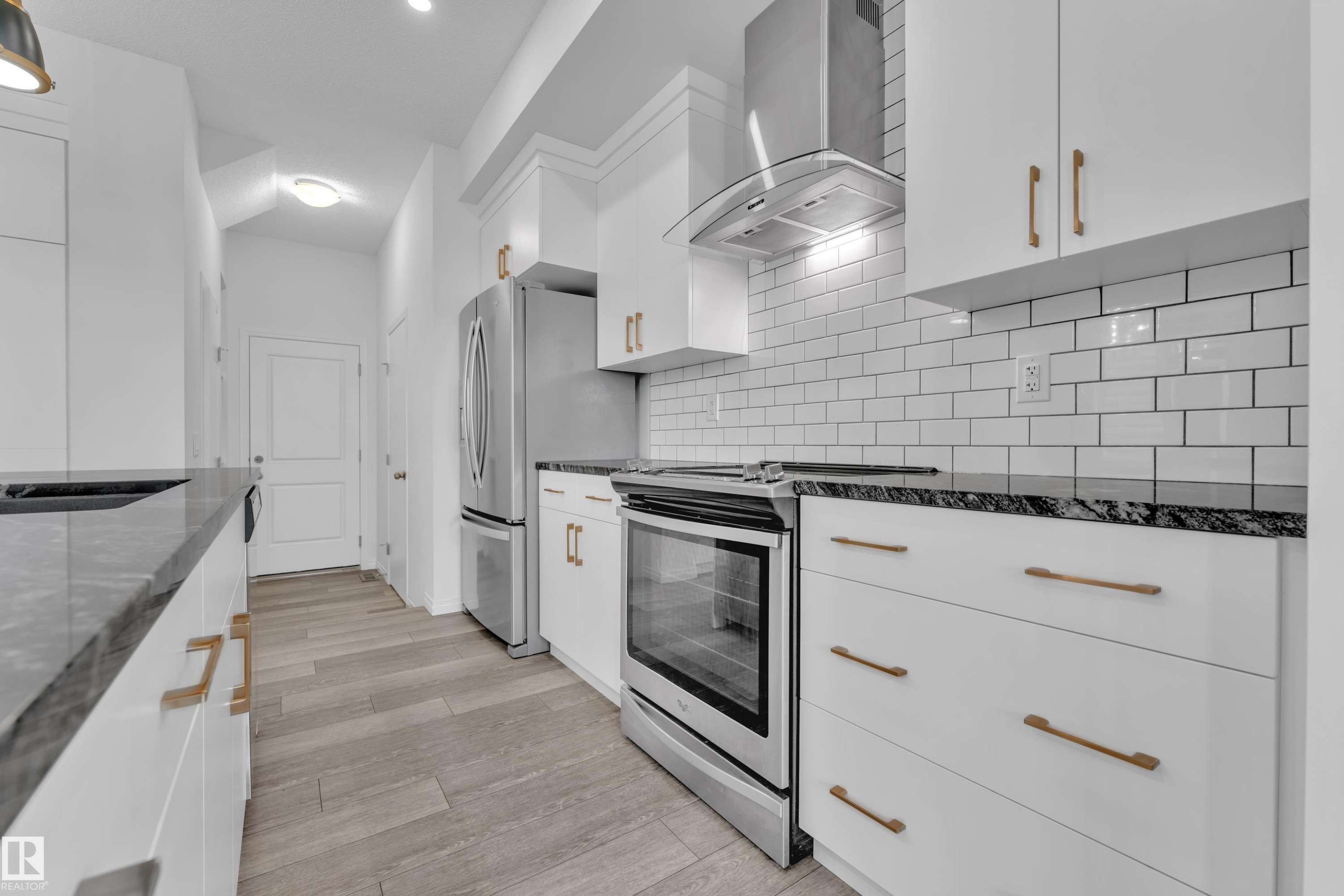 Contemporary kitchen featuring white cabinetry with brushed brass hardware, dark stone countertops, and a white subway tile backsplash - 144 Sunwapta Way, Edmonton, AB