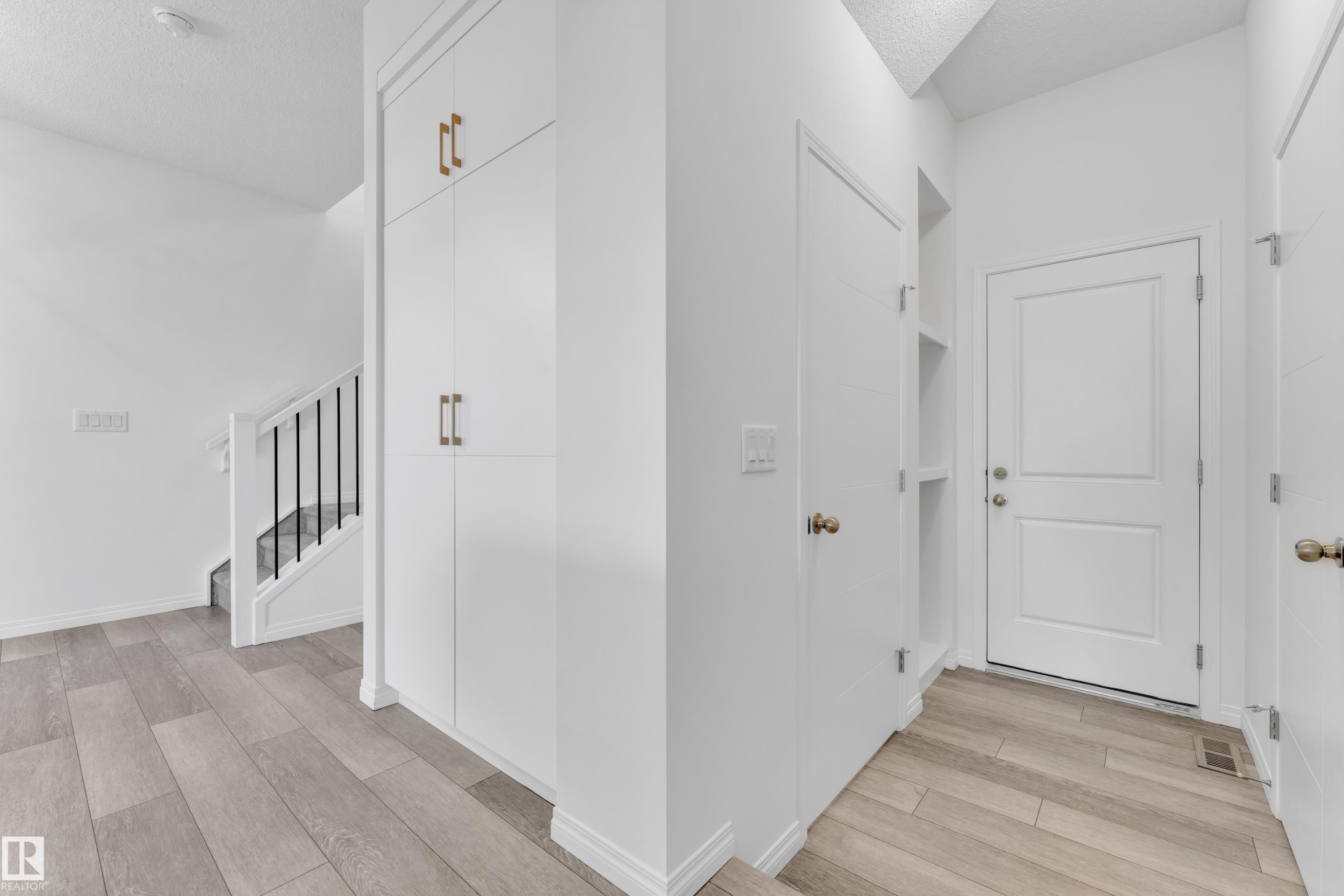 Entryway featuring wood-finish flooring, a white staircase with black metal balusters, built-in white cabinetry with brass-finish hardware, and a white paneled door - 144 Sunwapta Way, Edmonton, AB